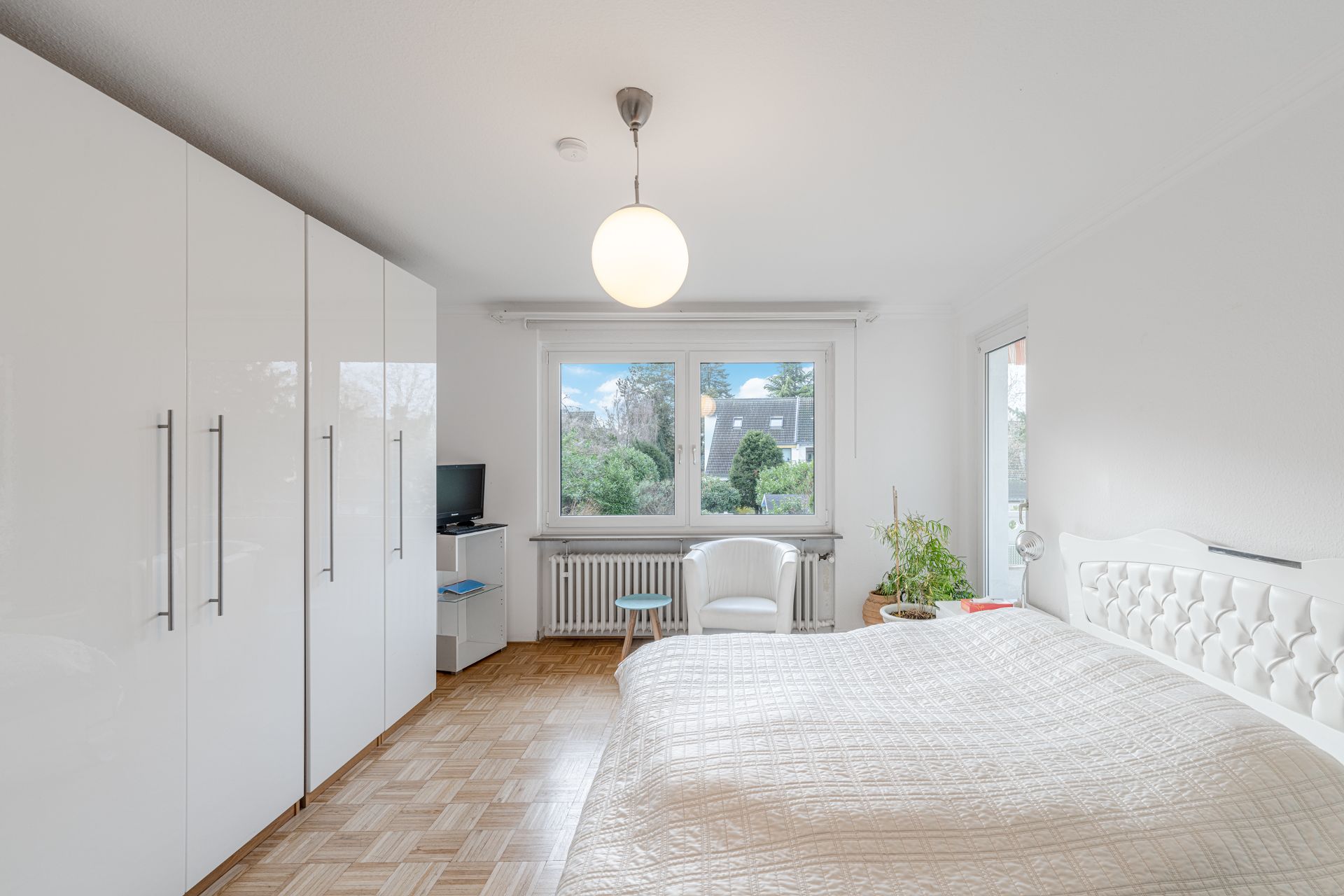 Helles Schlafzimmer mit großem weißen Schrank, Doppelbett und Fenster mit Blick ins Grüne.