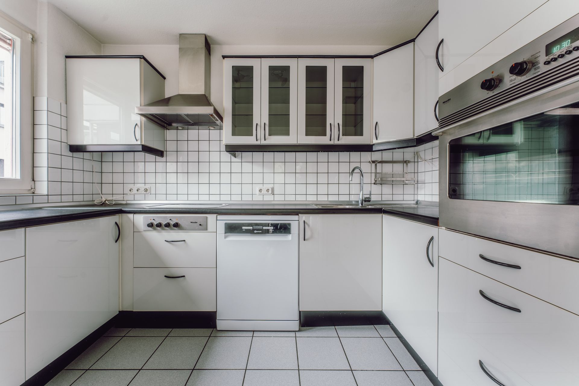 Moderne Einbauküche mit weißen Schränken, Geschirrspüler, Herd, Backofen und Fliesenspiegel.
