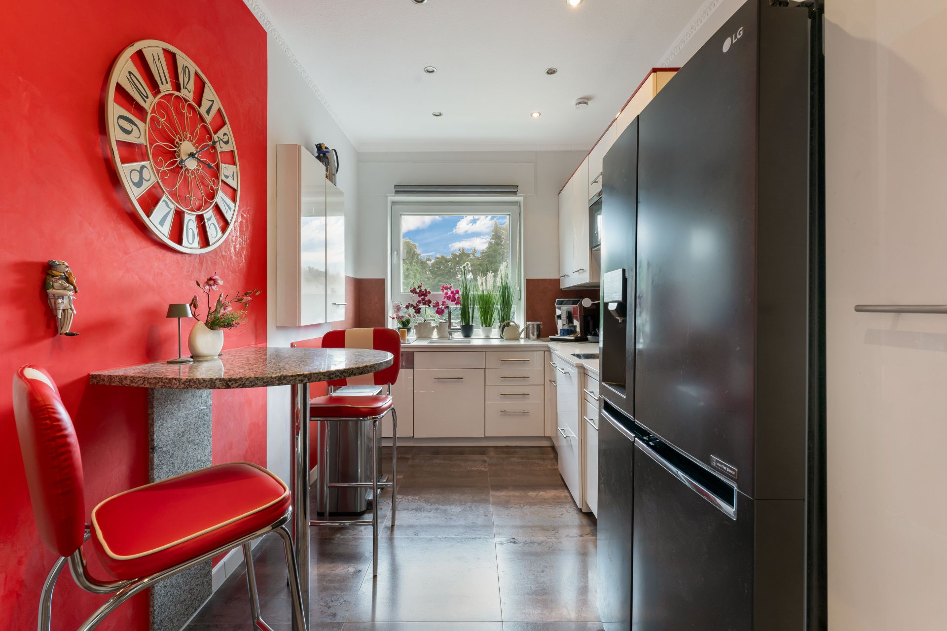 Moderne Küche mit schwarzem Kühlschrank, Bartisch, roten Stühlen und großem Wanduhren-Dekor.