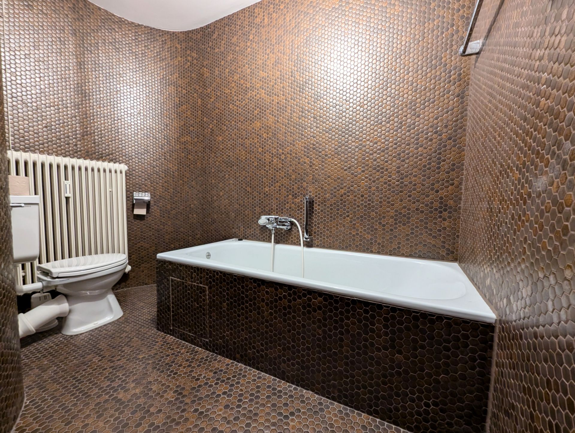 Badezimmer mit Badewanne, Toilette und braunen, runden Fliesen an Boden und Wänden.