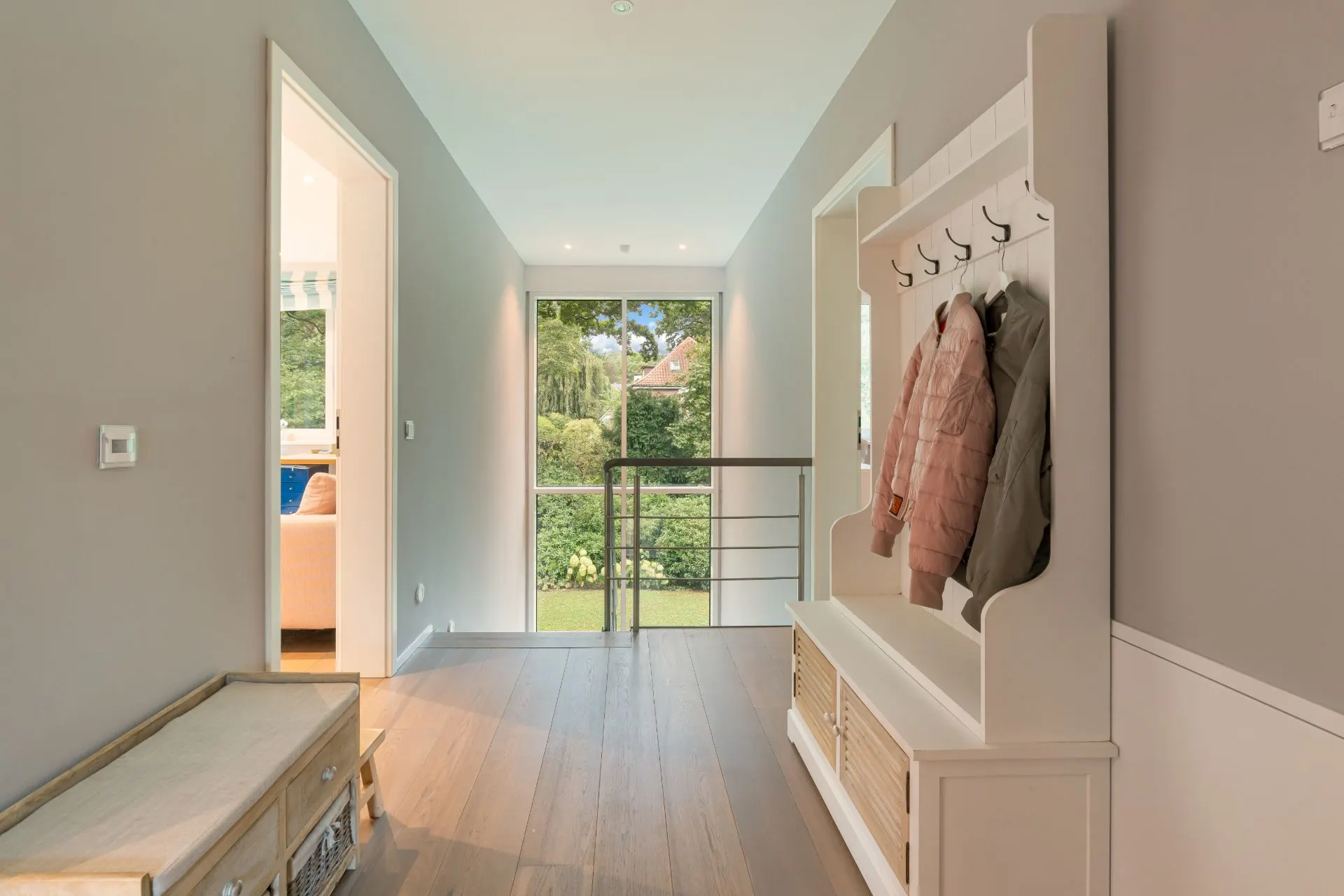 Heller Flur mit Garderobe, Holzboden und großem Fenster mit Blick ins Grüne.
