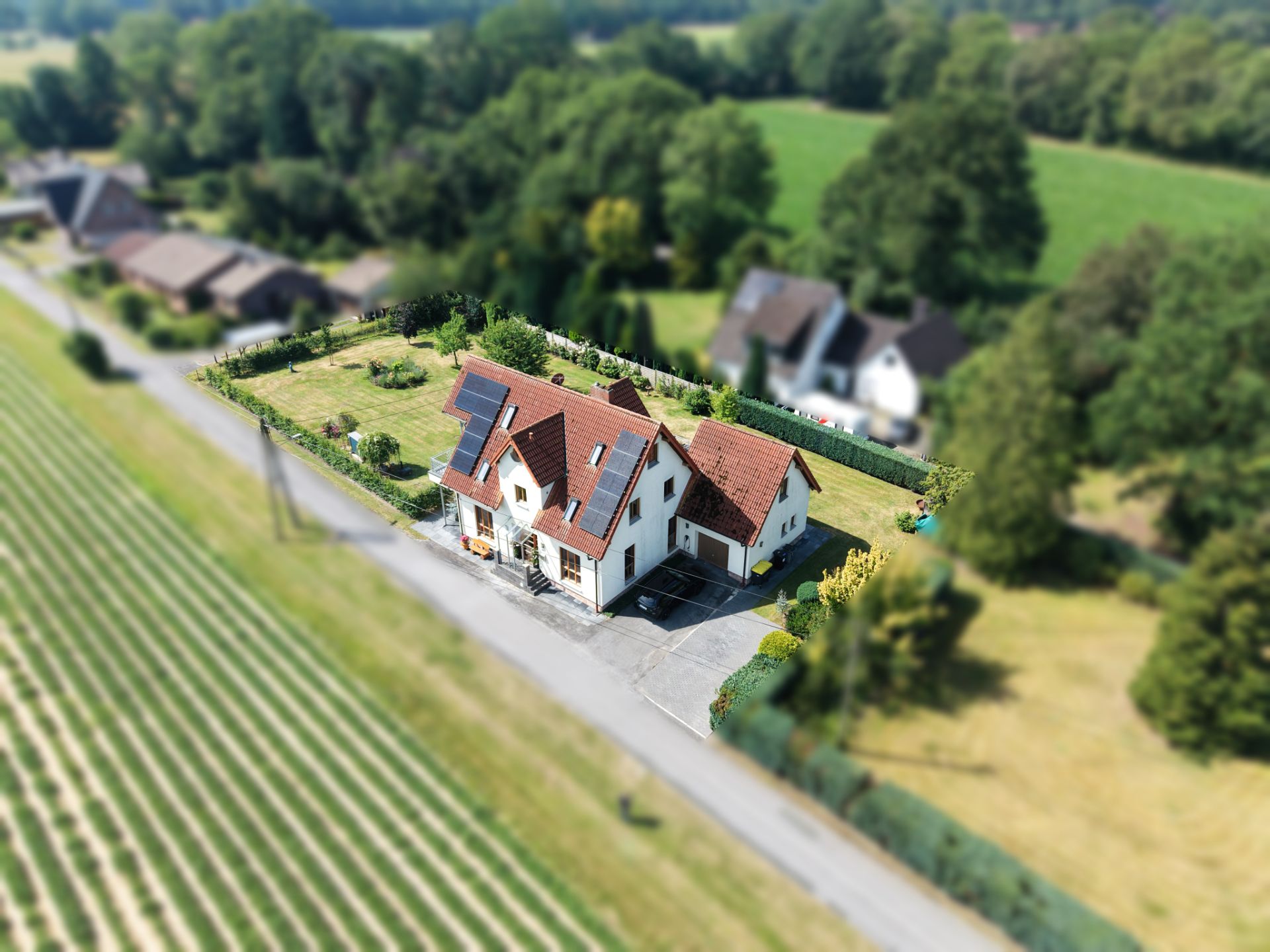 Luftaufnahme eines weißen Einfamilienhauses mit rotem Dach, Solarpanels und großem Garten.
