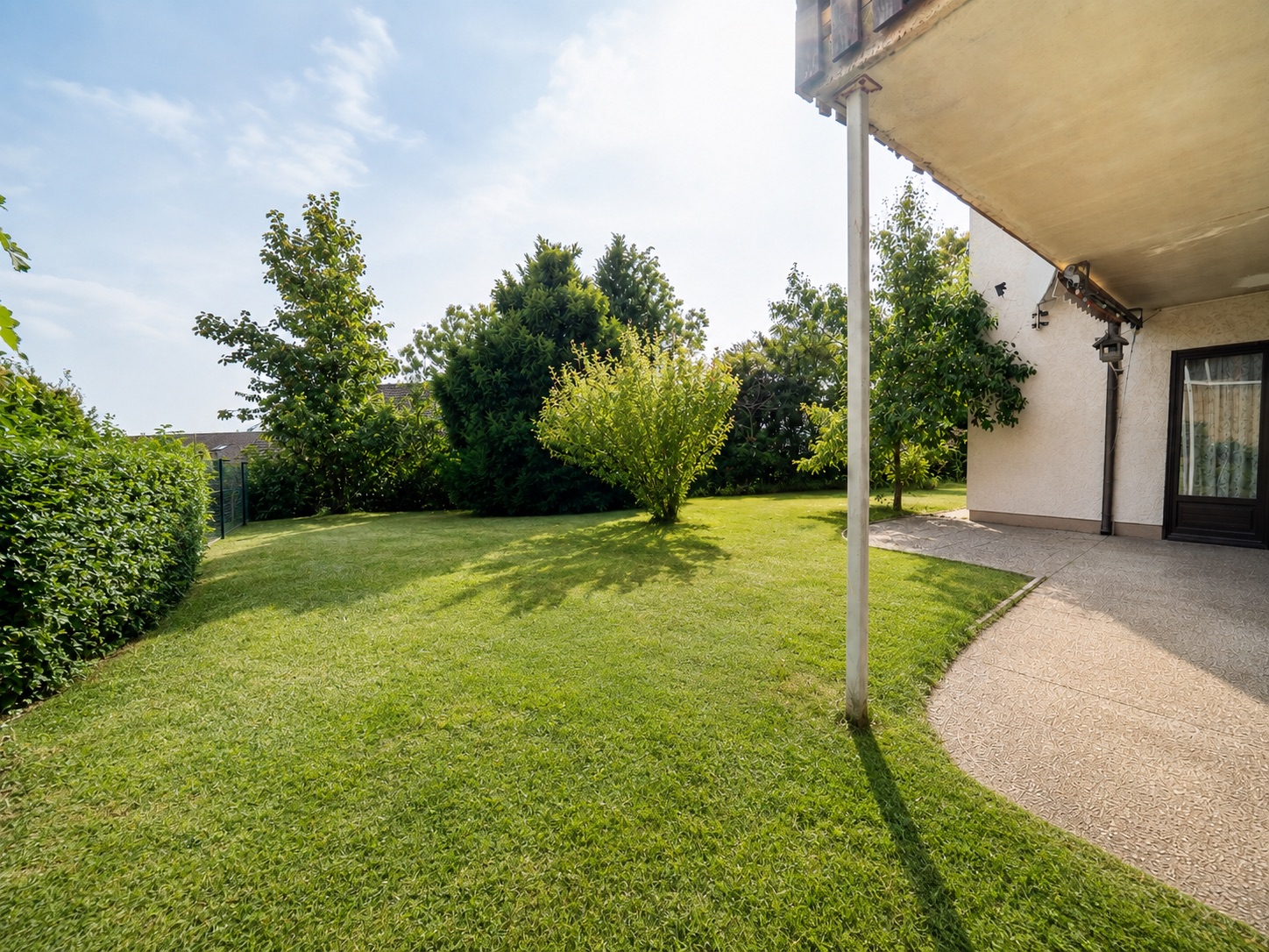 Garten mit Rasenfläche, Bäumen und überdachter Terrasse an einem Wohnhaus.