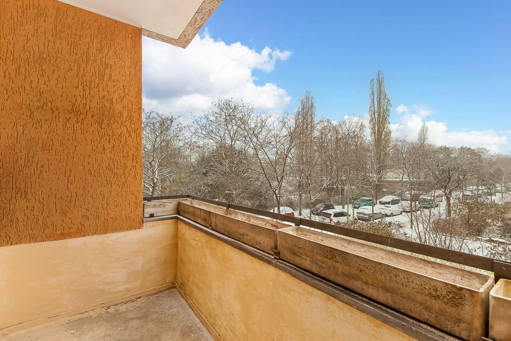 Balkon mit gelber Wand und Ausblick auf verschneite Bäume und geparkte Autos.