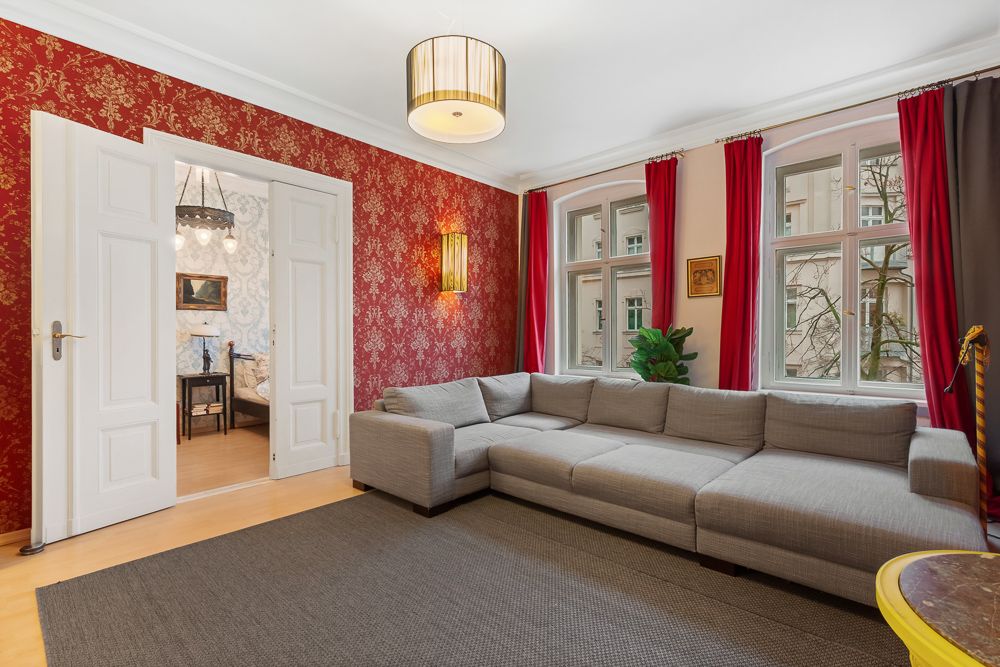 Wohnzimmer mit großer grauer Eckcouch, roten Vorhängen und roten Tapeten an einer Wand.