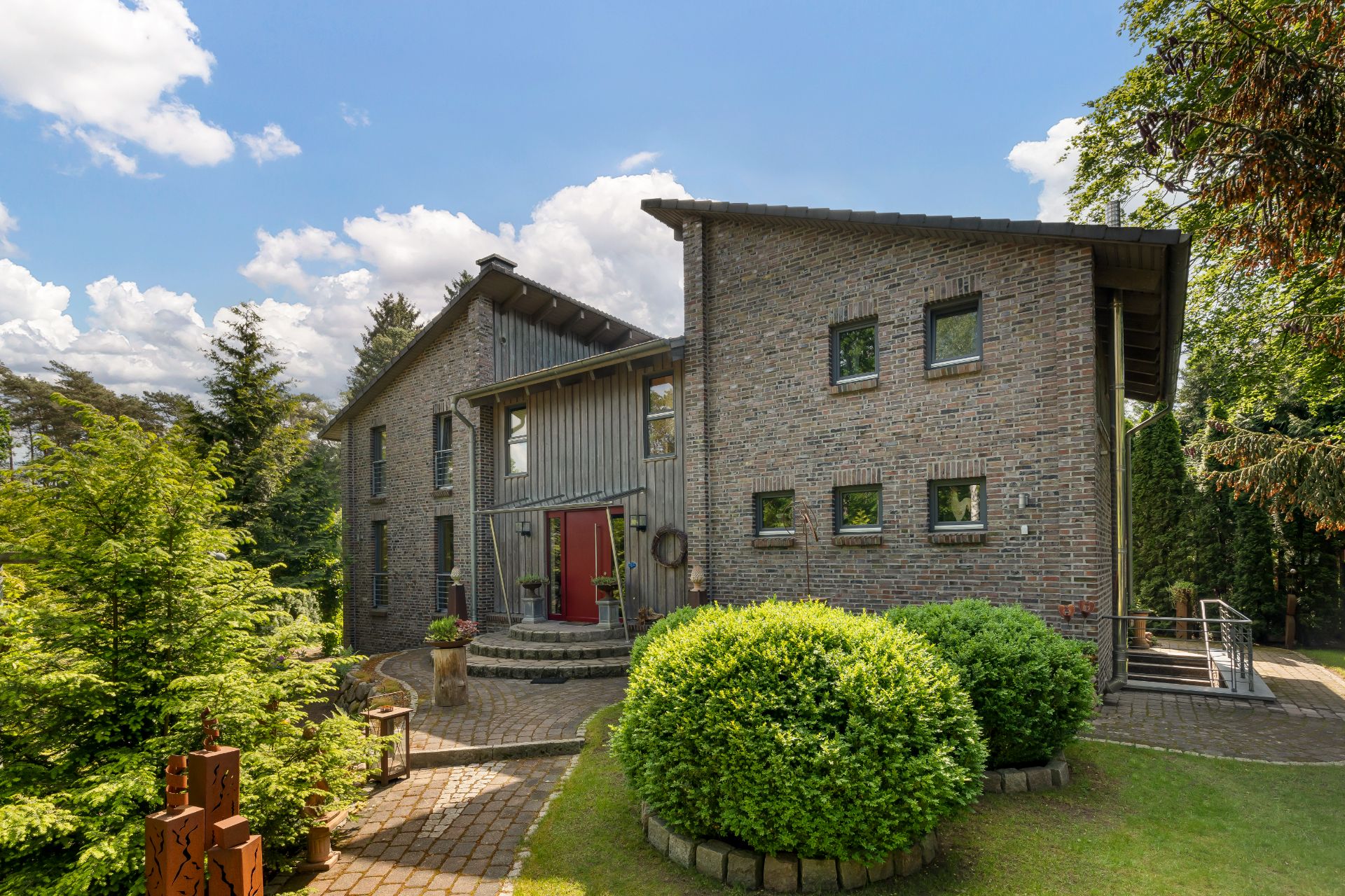 Modernes Backsteinhaus mit roten Türen, kleinen Fenstern und gepflegtem Garten vor dem Eingang.