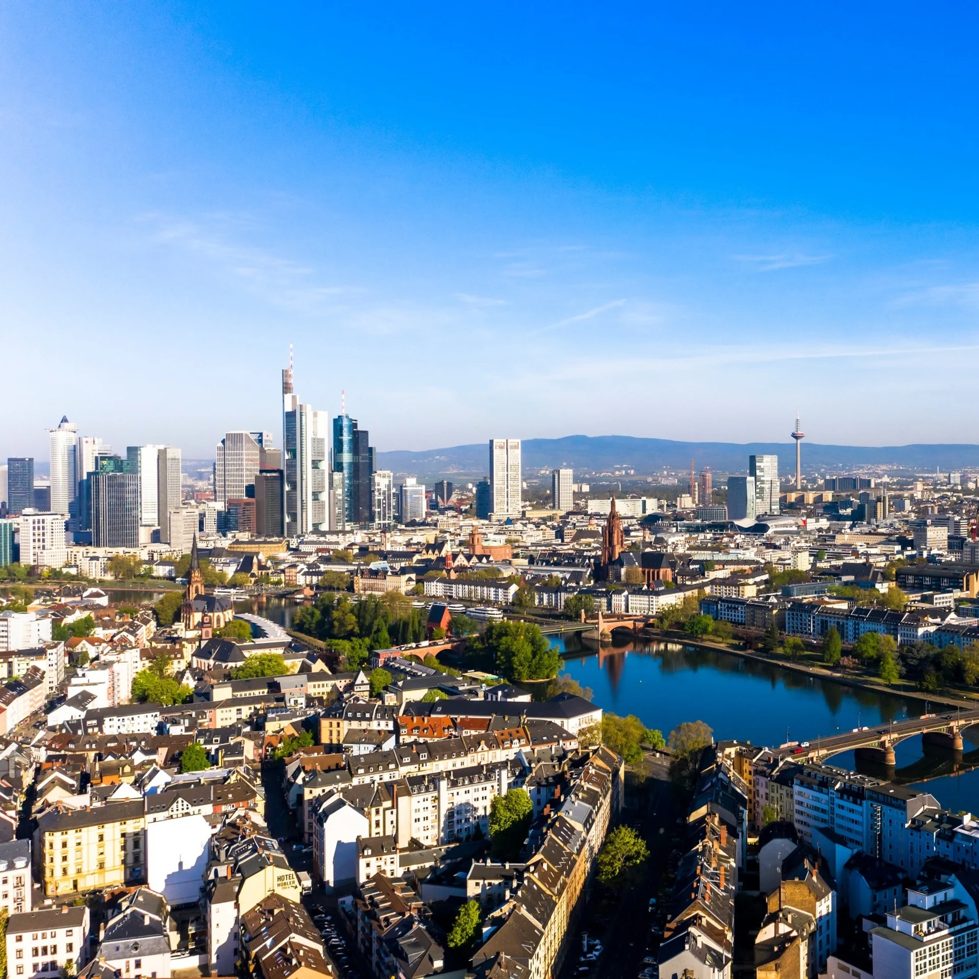 Stadtpanorama mit Fluss, Brücke, Wohnhäusern und Hochhäusern bei klarem Himmel.