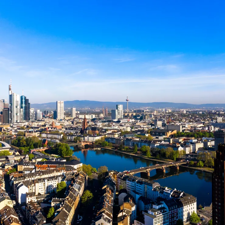 Stadtpanorama mit Fluss, Brücke, Wohnhäusern und Hochhäusern bei klarem Himmel.