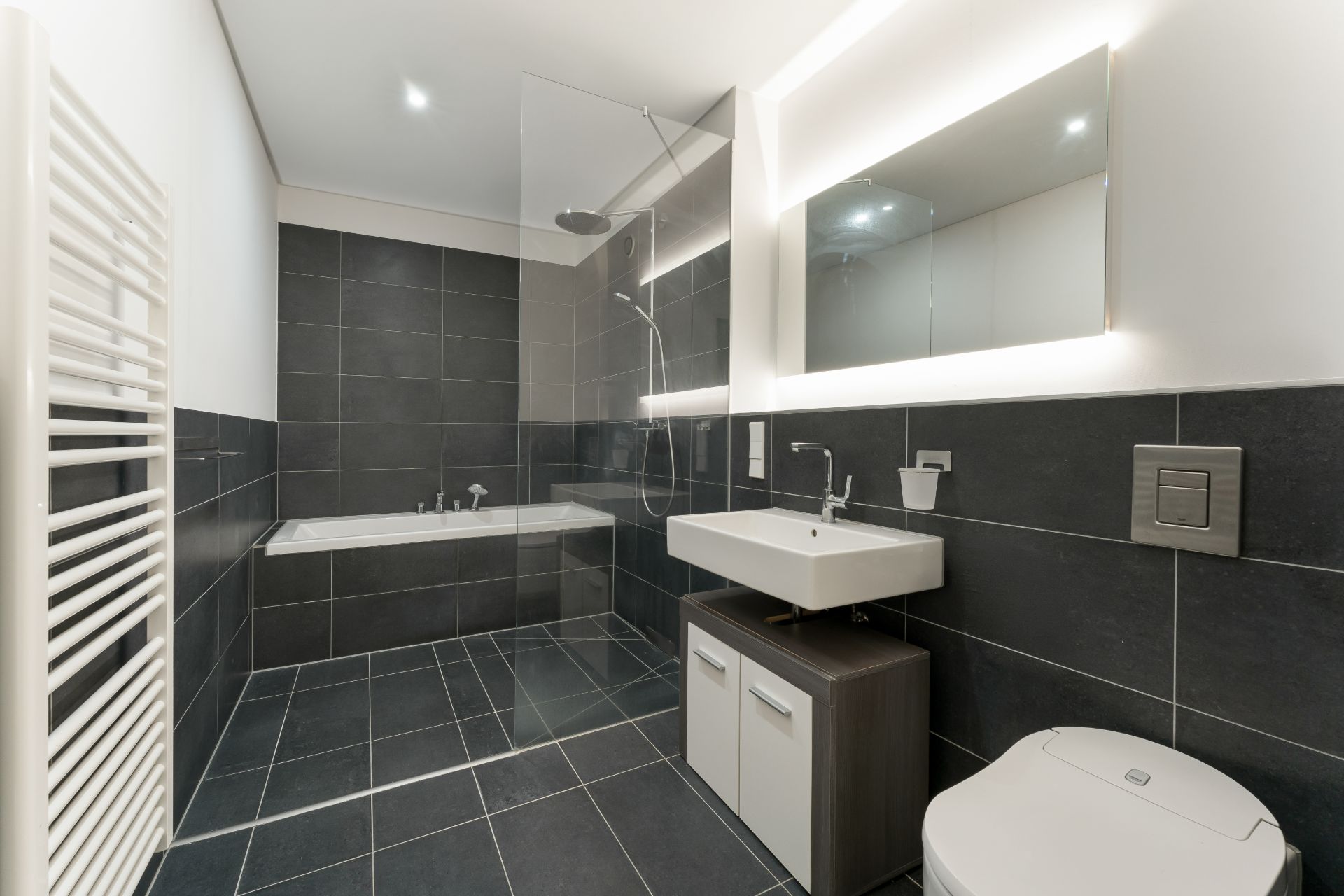 Modernes Badezimmer mit Dusche, Badewanne, Waschbecken und WC, schwarze Fliesen.