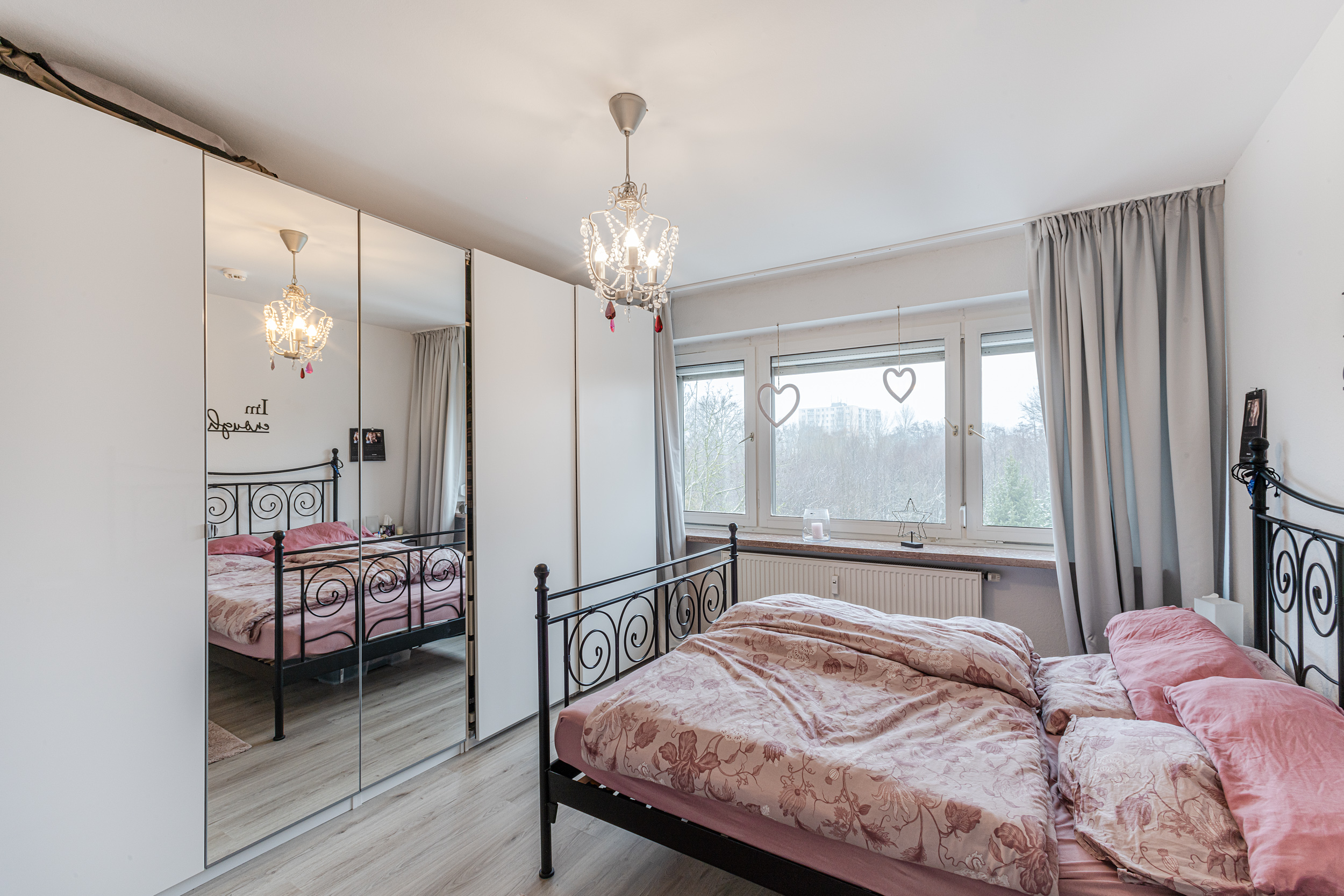 Helles Schlafzimmer mit Doppelbett, Spiegelkleiderschrank und großem Fenster mit Vorhängen.