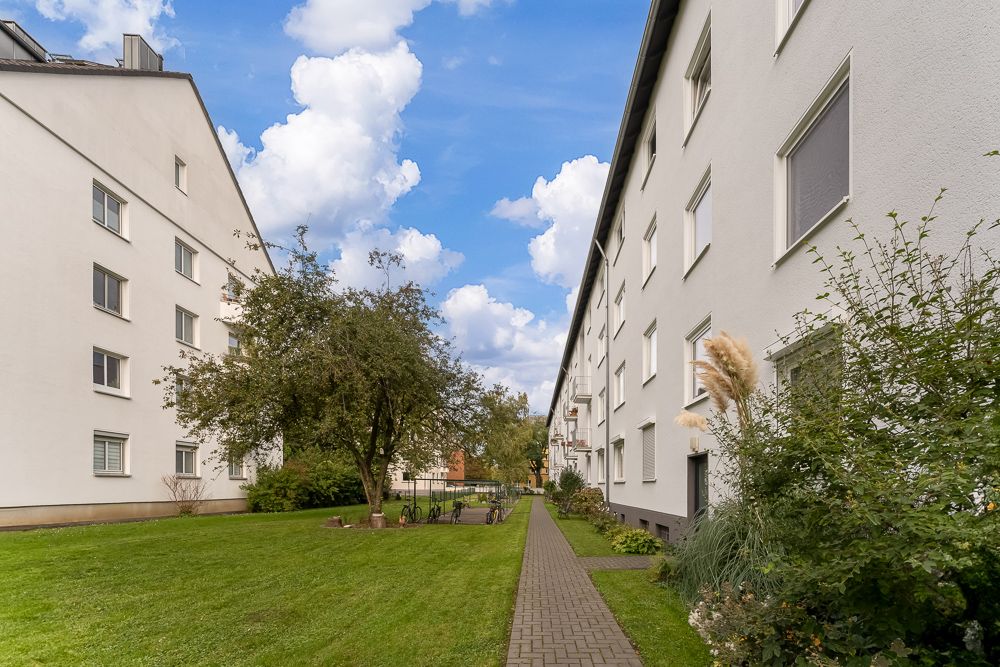 Gepflegter Weg zwischen zwei Wohngebäuden mit Rasen, Bäumen und Fahrrädern.