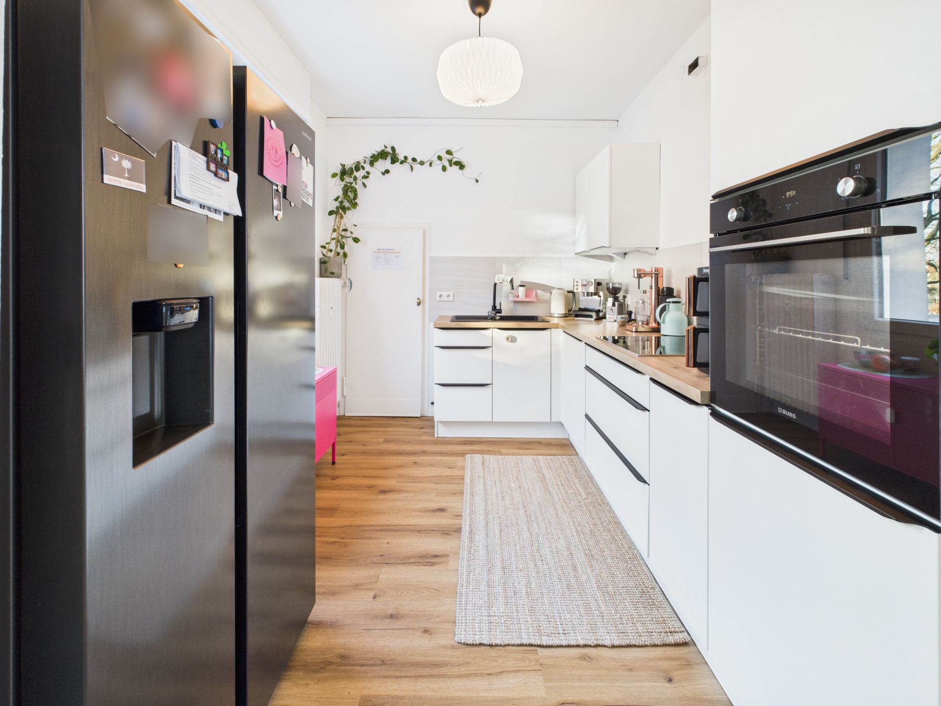 Moderne Küche mit weißen Schränken, Holzfußboden, großem Kühlschrank und eingebautem Backofen.