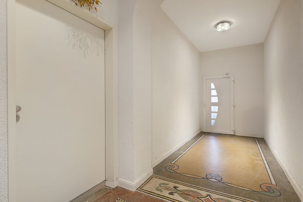 Heller Flur mit weißer Tür, verziertem Boden und moderner Eingangstür.