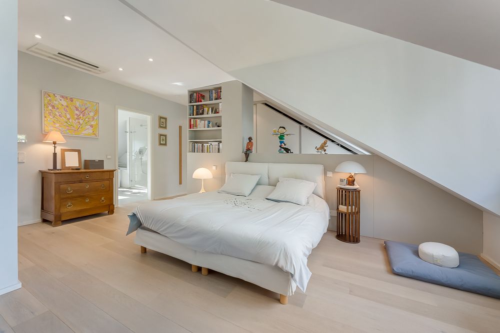 Helles Schlafzimmer mit Doppelbett, Nachttischen, Kommode, Bücherregal und Dachschräge.