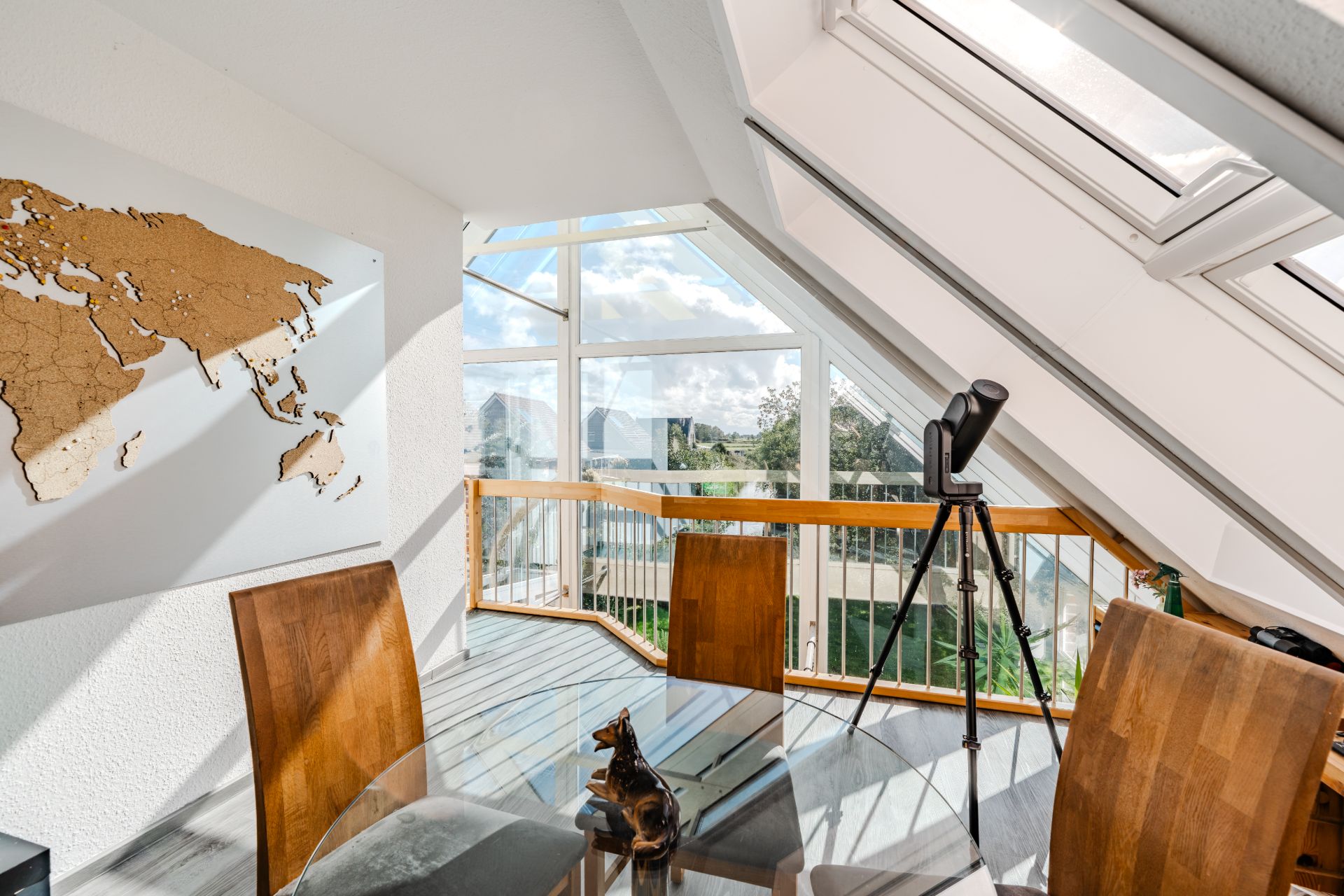 Essbereich mit Glastisch, Holzstühlen, Weltkarte und Fernglas vor großen Fenstern im Dachgeschoss.
