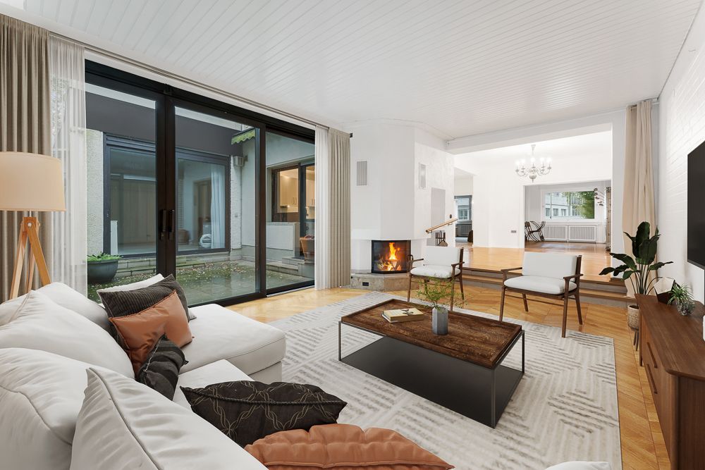 Helles Wohnzimmer mit Kamin, Sofa, Couchtisch und Blick auf Innenhof durch große Glas-Schiebetüren.