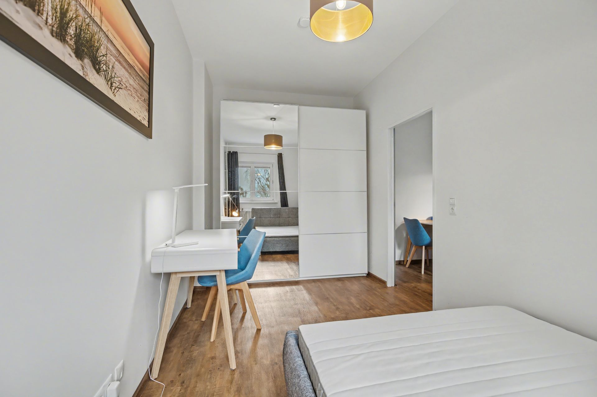 Helles Schlafzimmer mit Schreibtisch, Kleiderschrank und Bett, Holzboden und Wandbild.