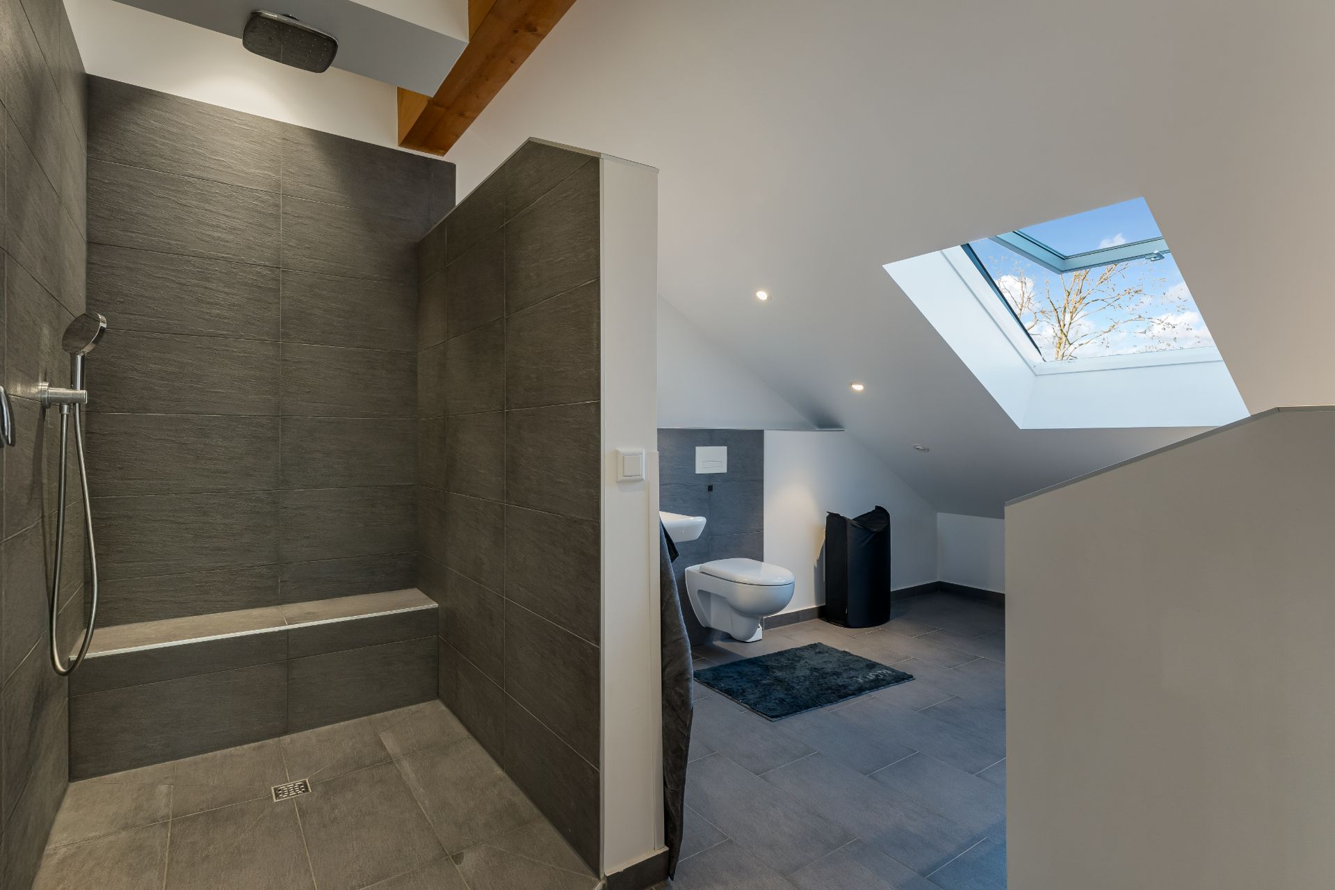 Modernes Badezimmer mit offener Dusche, WC und großem Dachfenster unter einer Dachschräge.