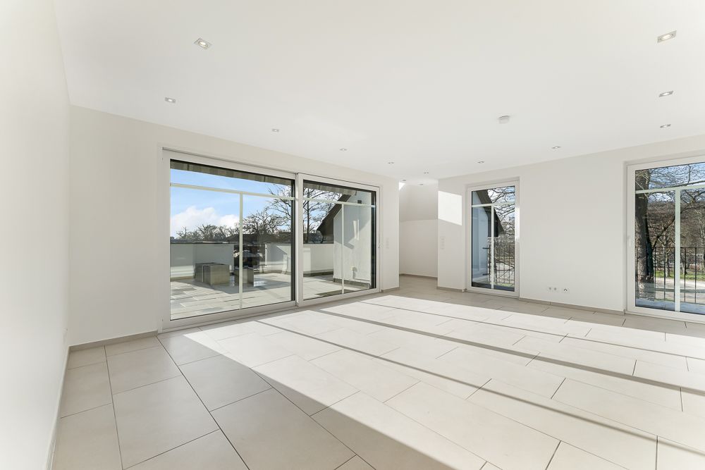 Heller, leerer Wohnraum mit großen Fenstern und Zugang zur Terrasse.