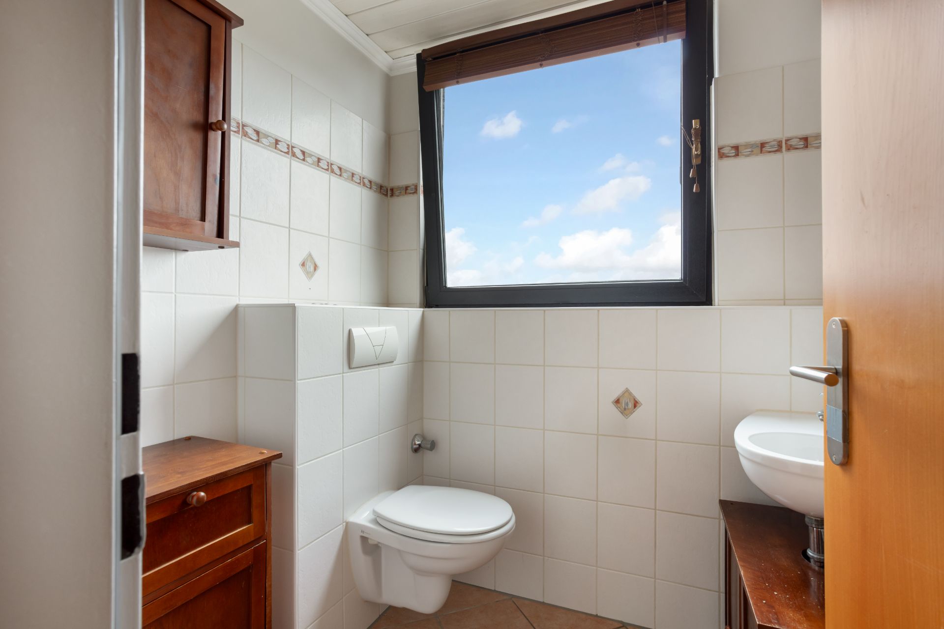 Kleines Badezimmer mit Wandtoilette, Waschbecken und Fenster mit Blick auf den Himmel.