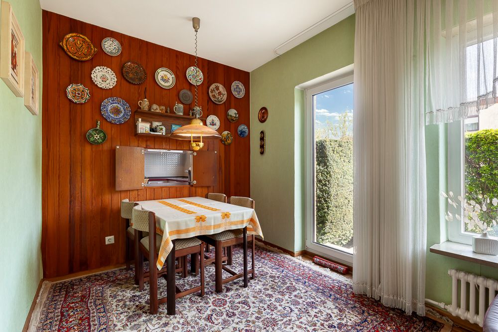 Esszimmer mit Holzwand, Esstisch, Teppich und Fenster mit Blick in den Garten.