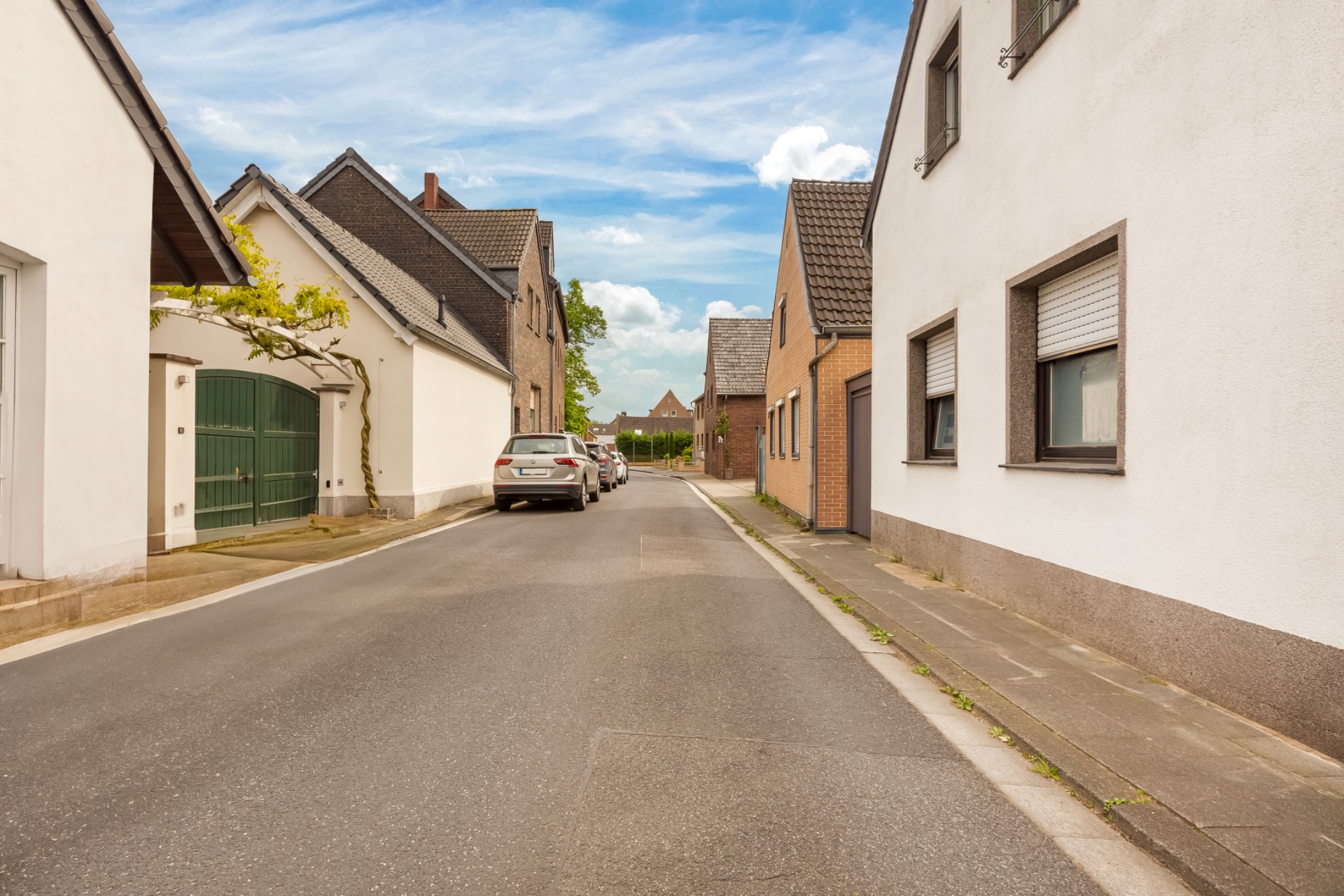 Schmale Wohnstraße mit parkenden Autos und Häusern auf beiden Seiten bei Tageslicht.