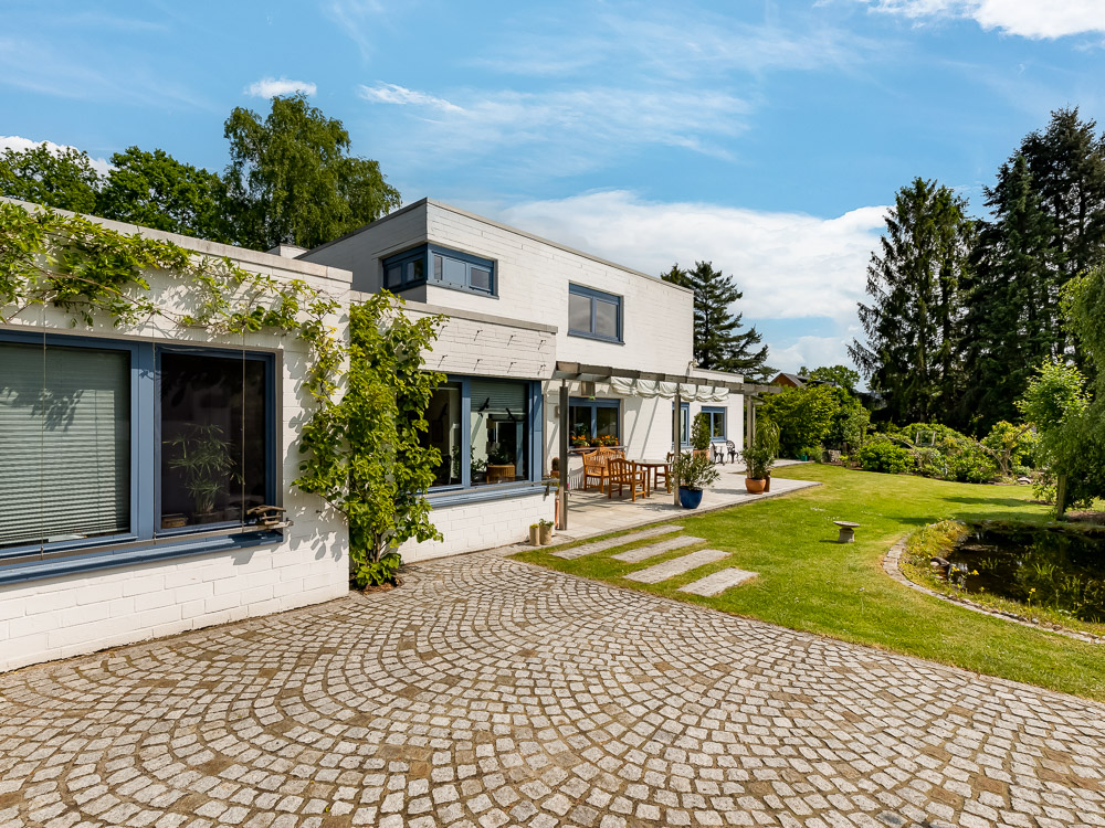 Modernes Wohnhaus mit Terrasse, Gartenmöbeln, Steinweg und gepflegtem Garten.