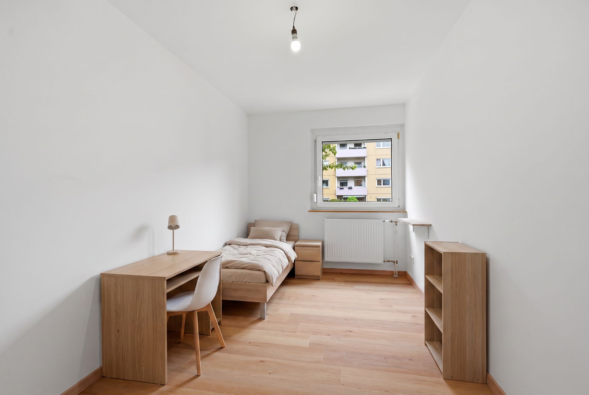 Helles Schlafzimmer mit Einzelbett, Schreibtisch, Stuhl, Regal und Fenster. Holzfußboden.