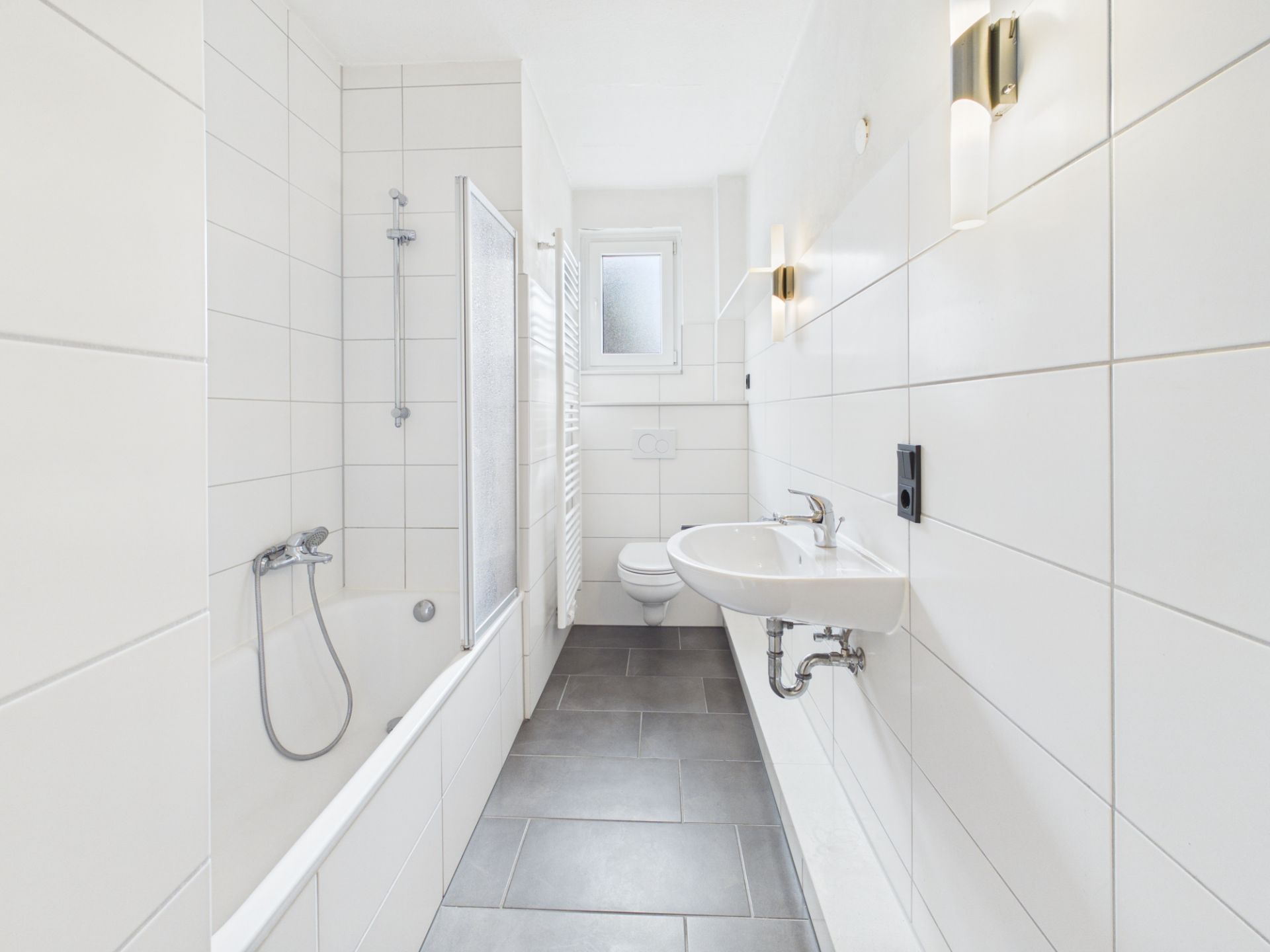 Helles Badezimmer mit Badewanne, Wandwaschbecken, WC und Fenster.