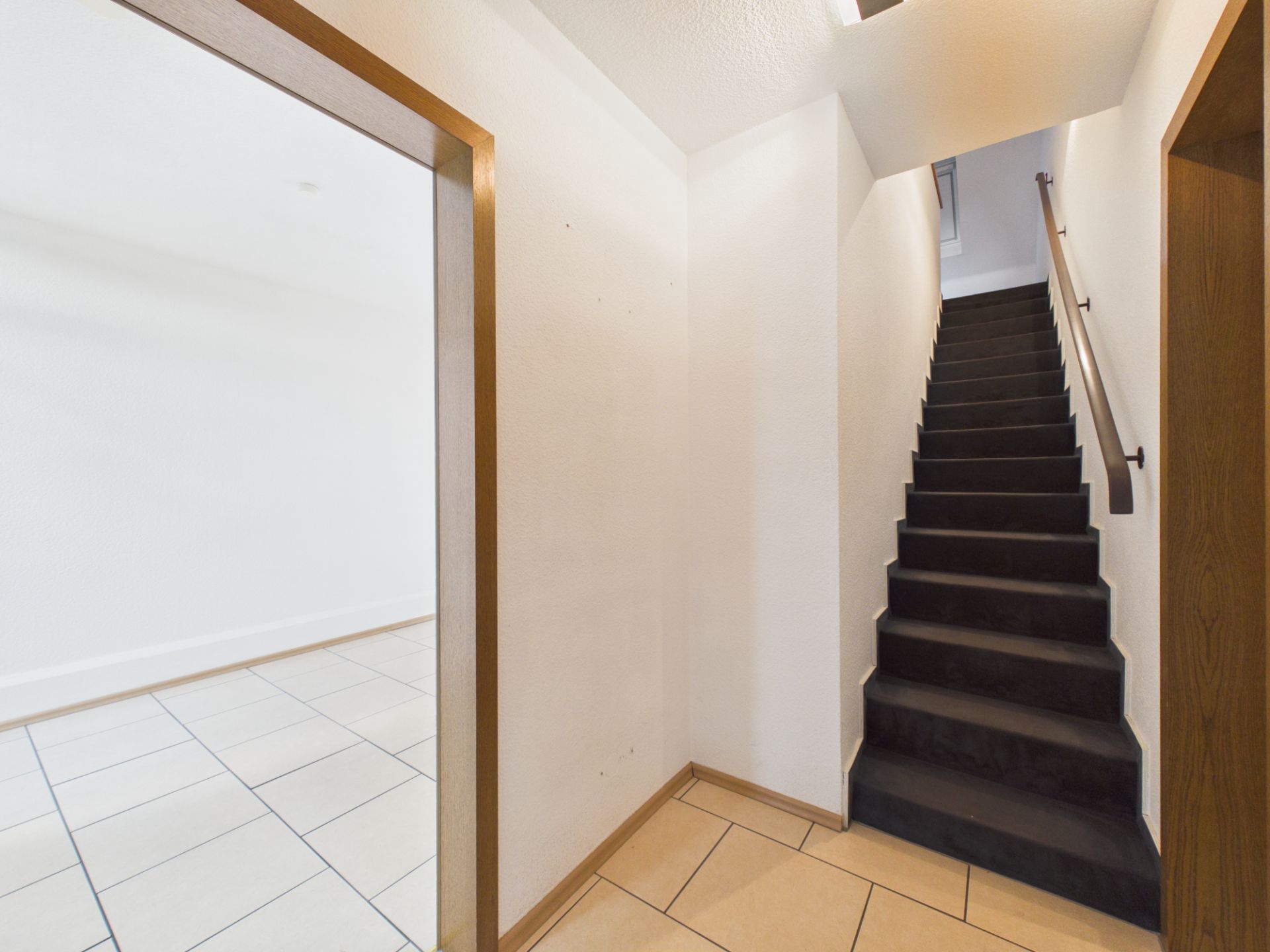 Heller Flur mit Fliesenboden und einer schwarzen Treppe nach oben.