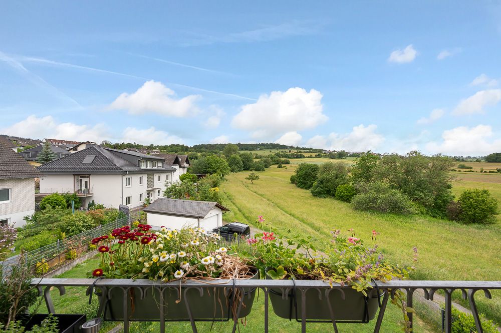 Aussicht vom Balkon auf Wiesen, Häuser und einen Blumenkasten.