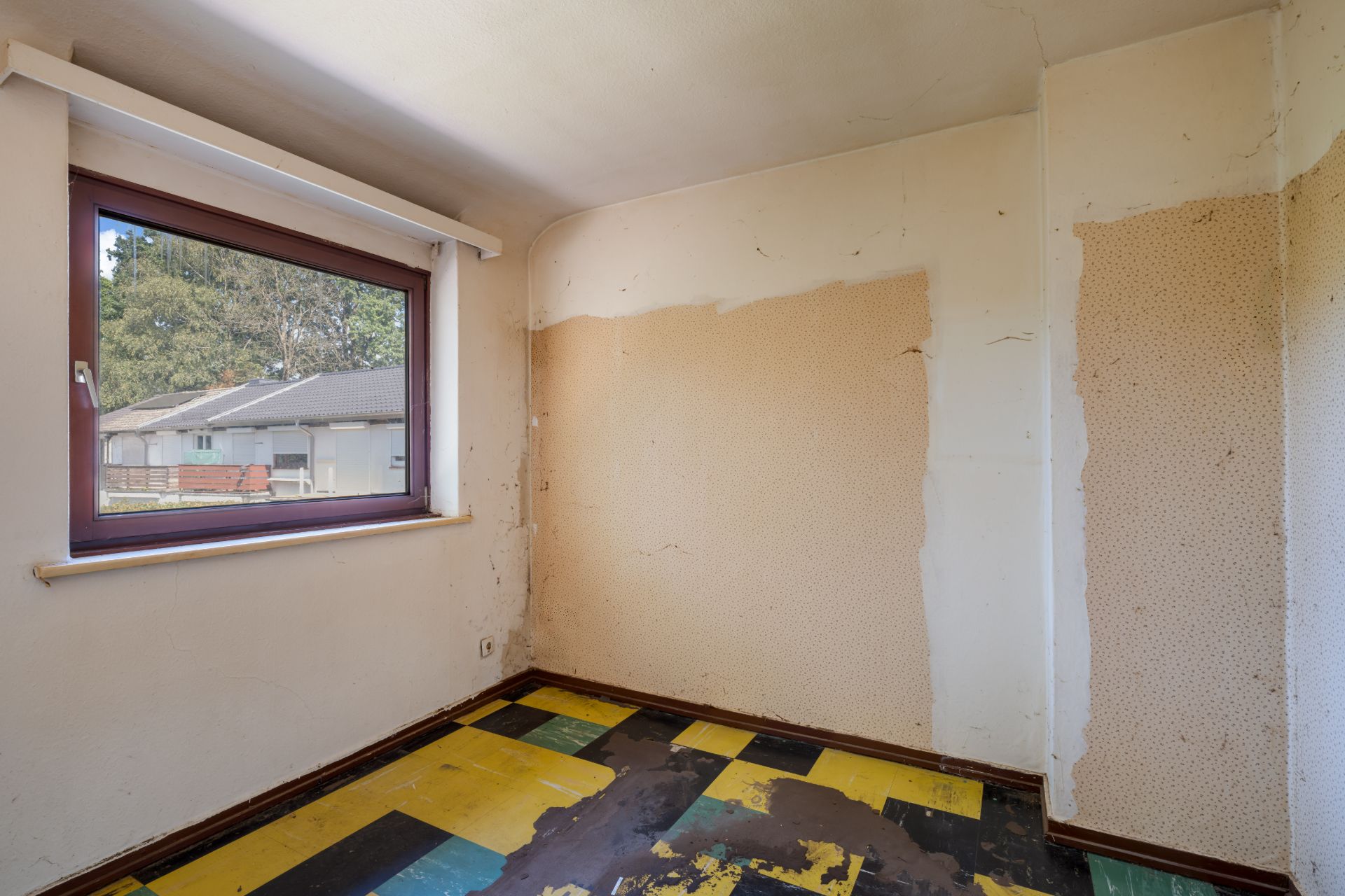 Kleiner leerer Raum mit abgenutztem Boden und einem Fenster, das nach draußen zeigt.