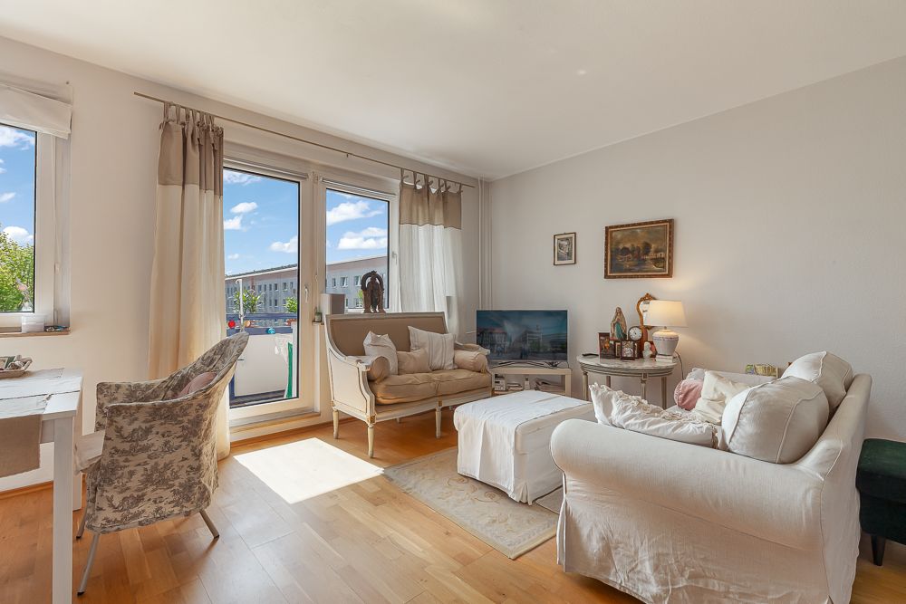 Helles Wohnzimmer mit Sofa, Sessel, Couchtisch, Fernseher und großen Fenstern.
