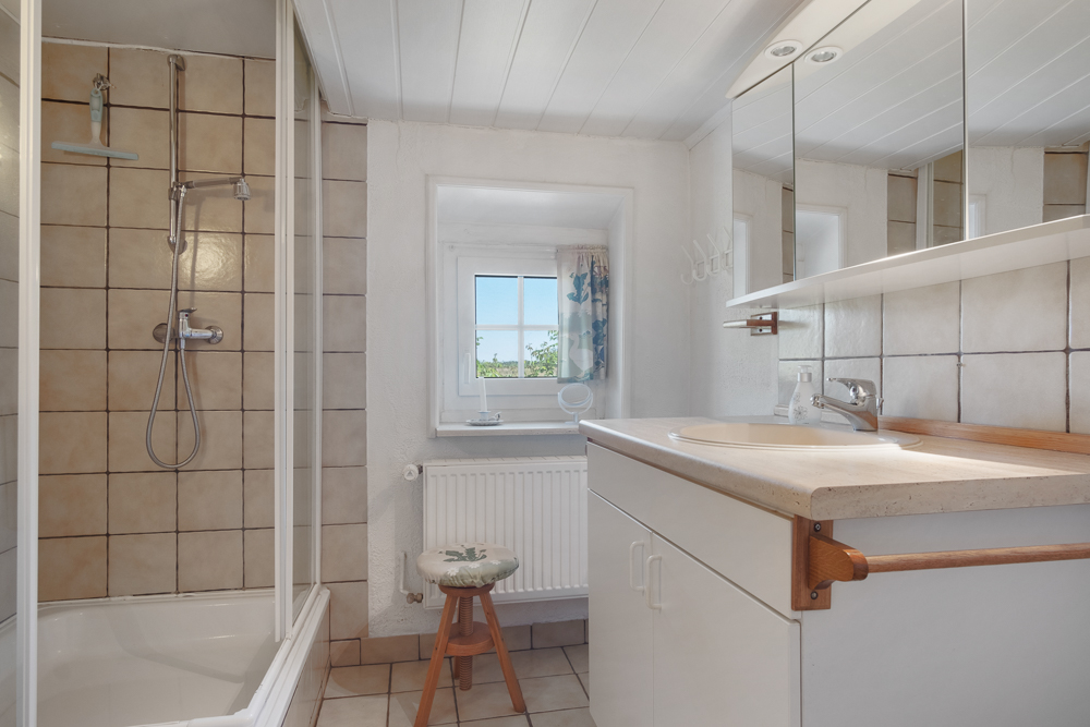 Helles Badezimmer mit Dusche, Waschbecken, Spiegel und Fenster.