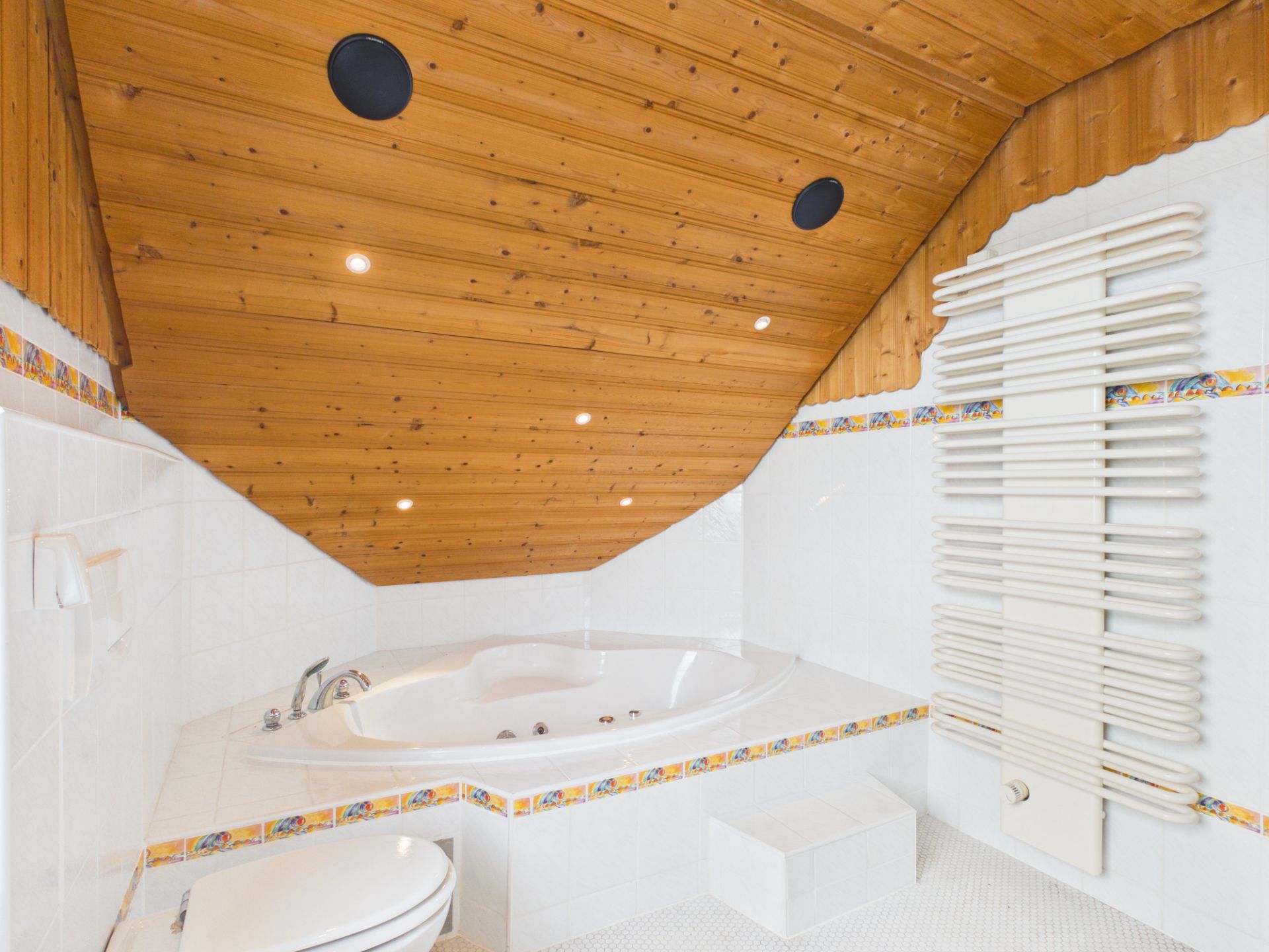 Modernes Badezimmer mit Eckbadewanne, schräger Holzdecke und weißem Wandheizkörper.