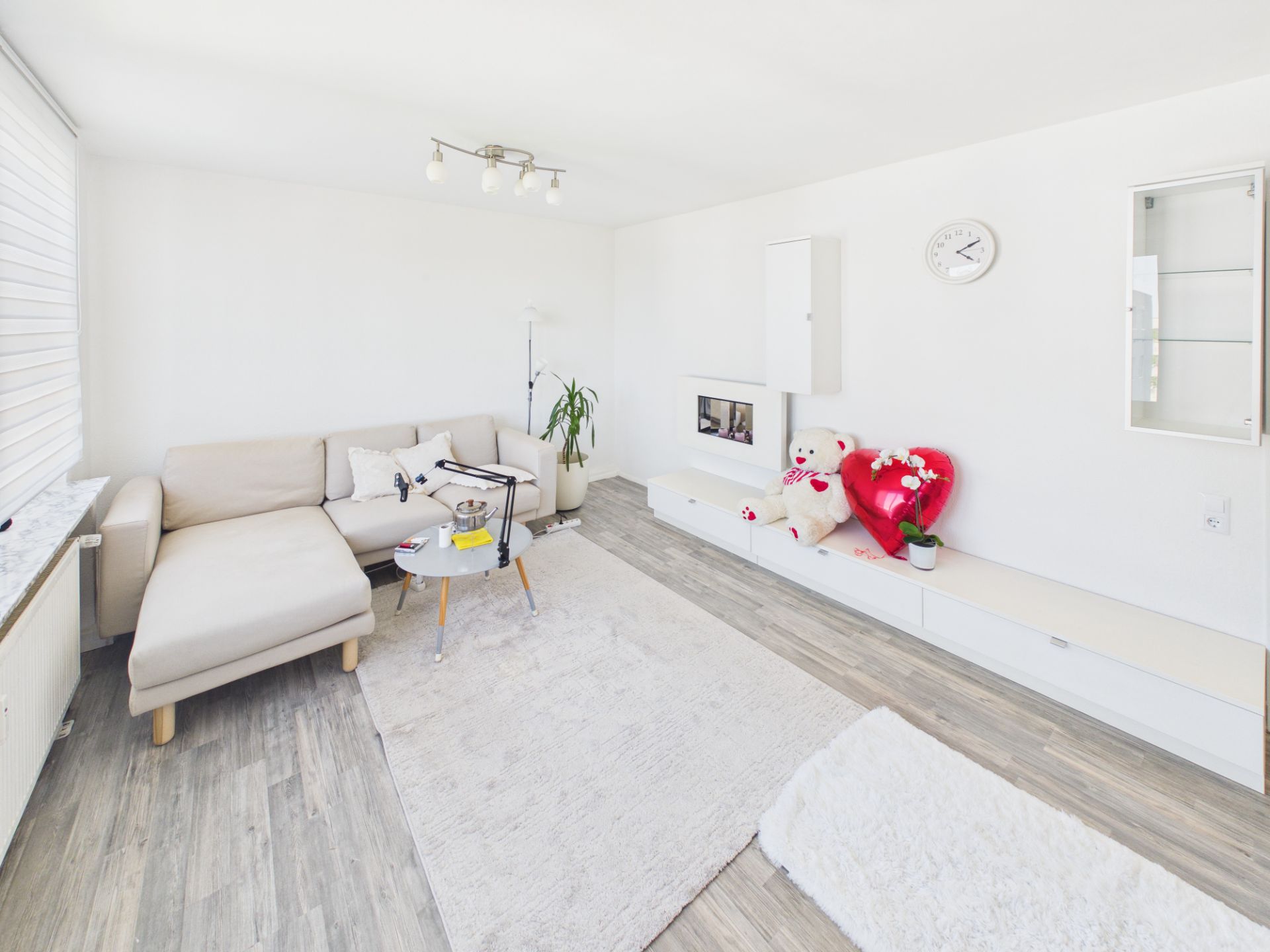Helles Wohnzimmer mit Ecksofa, Couchtisch, Teppich und Dekoration auf weißem Boden.
