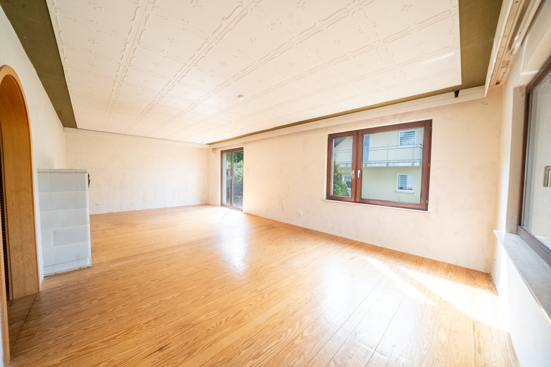 Helles, leeres Wohnzimmer mit Parkettboden, weißen Wänden und großen Fenstern.