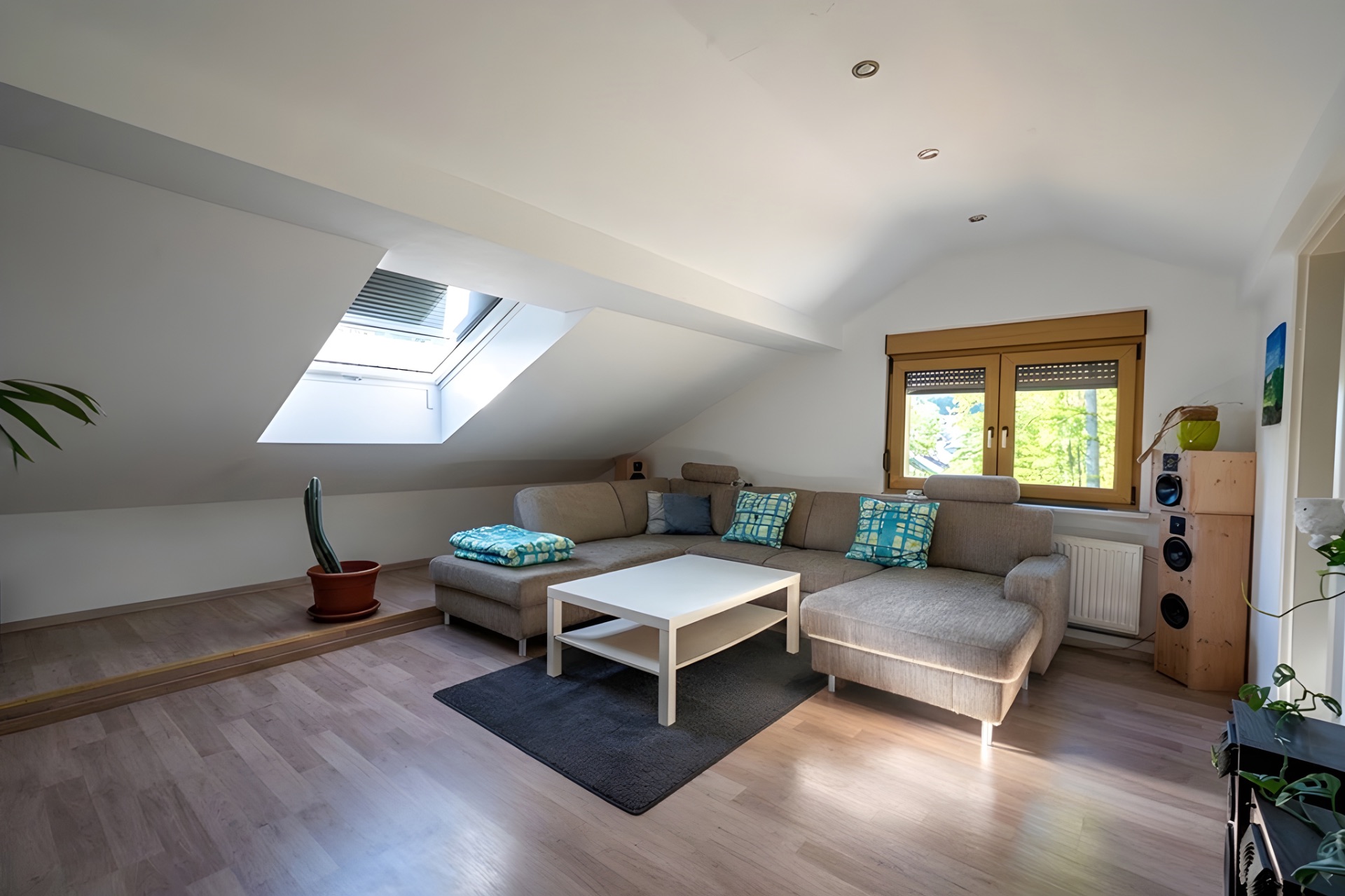 Wohnzimmer mit Ecksofa, Couchtisch, Dachfenster und Holzboden unter einer Schräge.