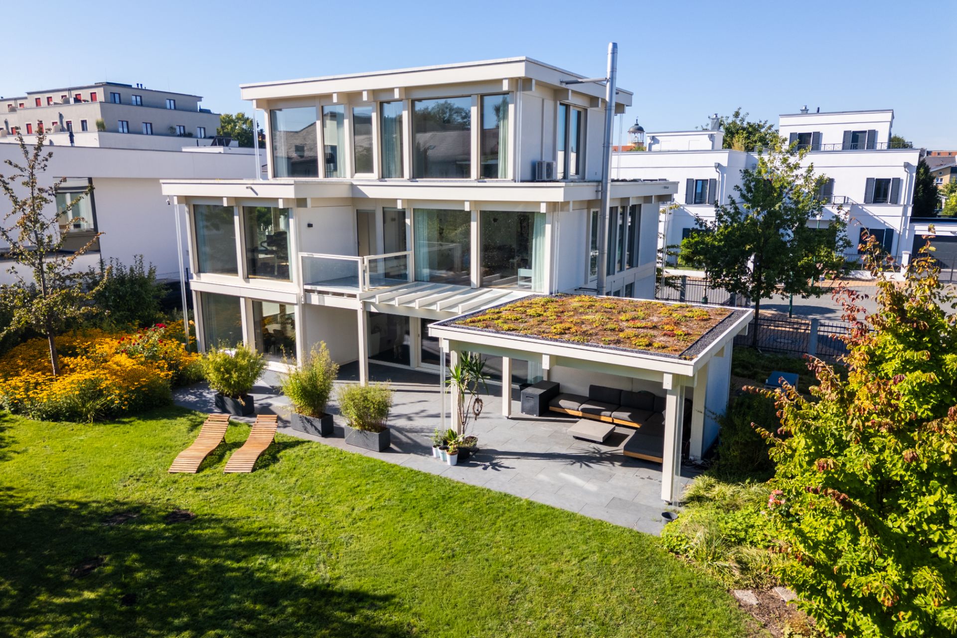 Modernes Wohnhaus mit großen Fenstern, Terrasse und begrüntem Dach im Garten.
