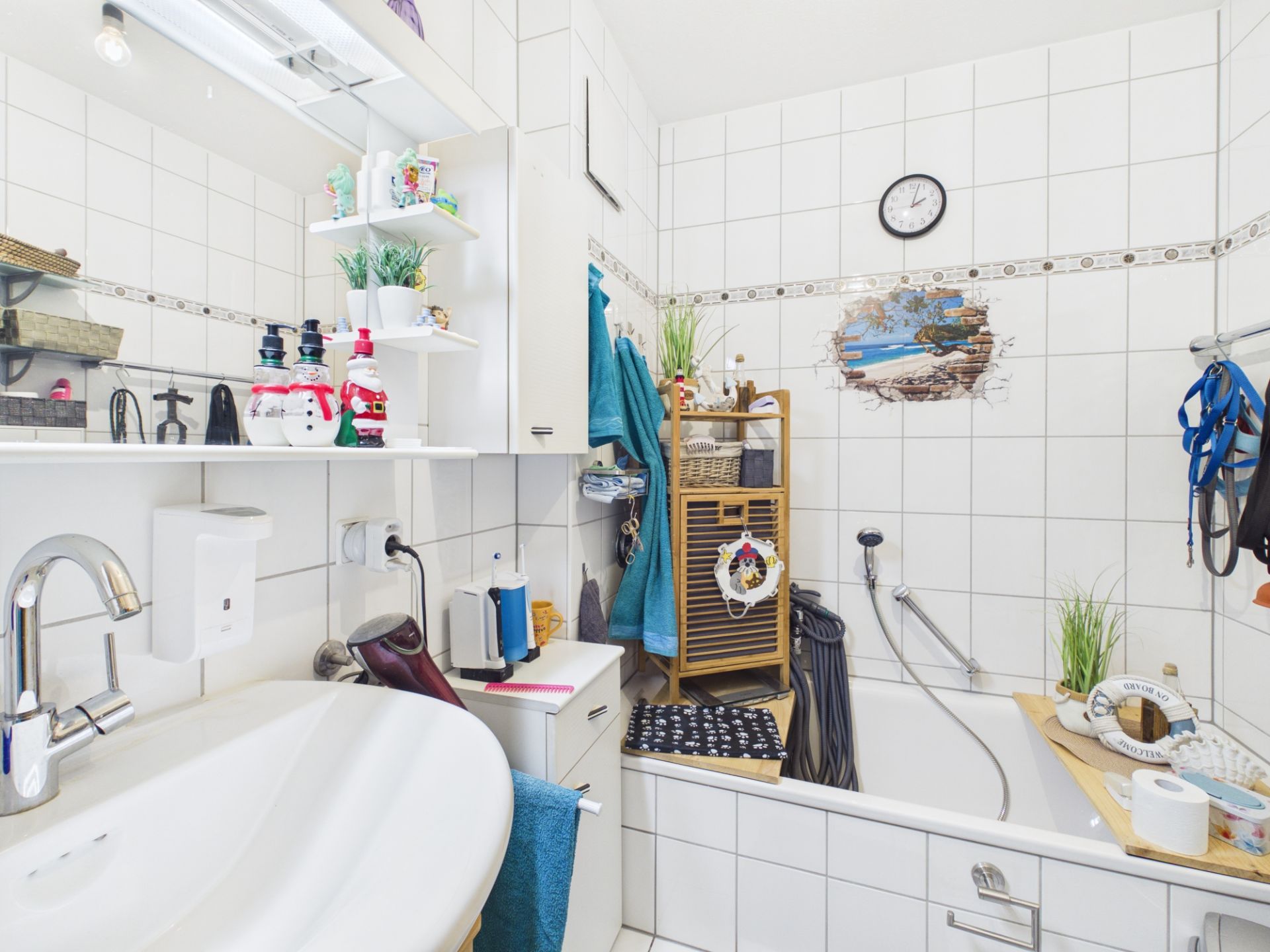 Weiß gefliestes Badezimmer mit Badewanne, Waschbecken, Regal, Pflanzen und Uhr an der Wand.