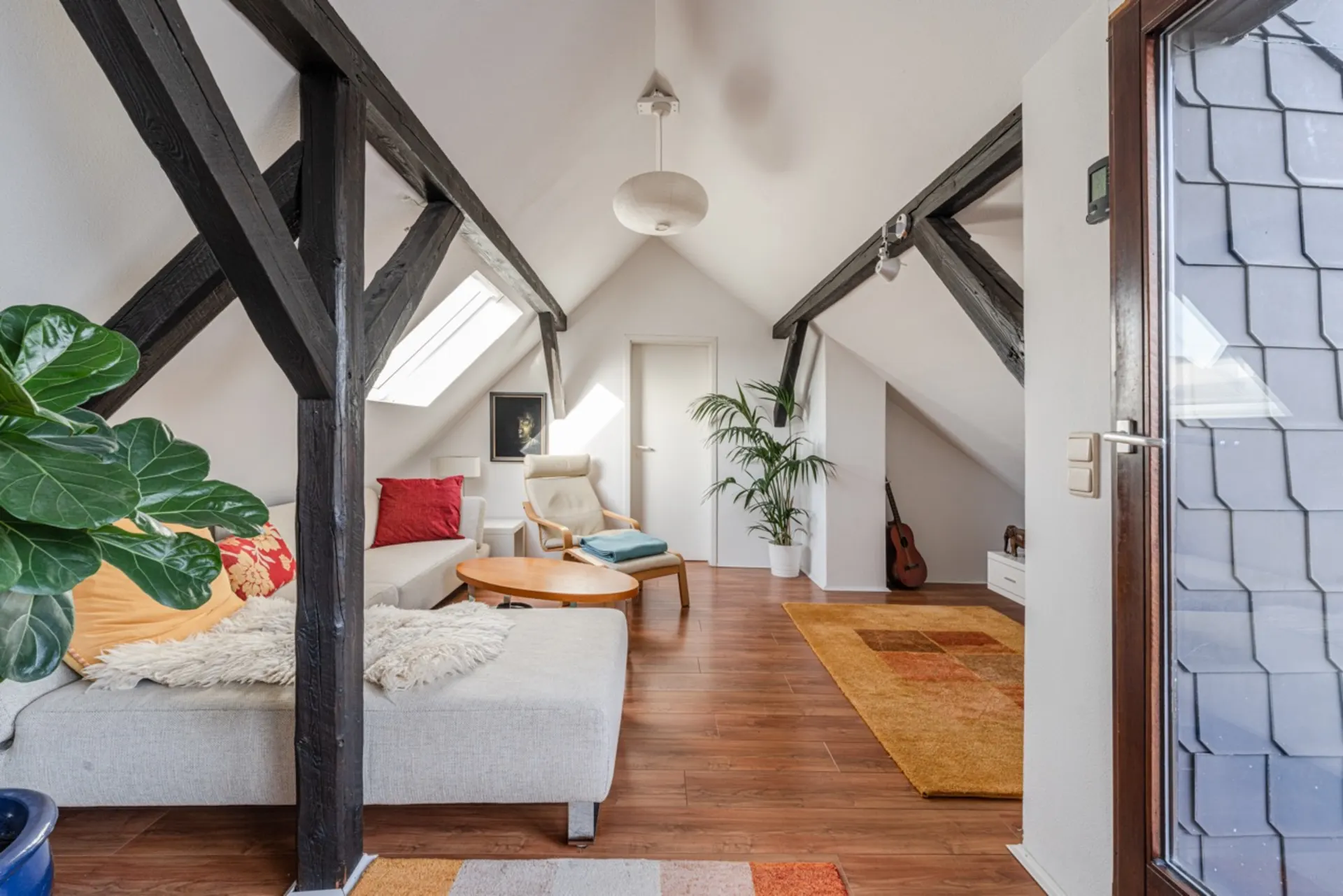 Helles Wohnzimmer im Dachgeschoss mit Sofa, Sessel, Pflanzen und Gitarre auf Holzboden.