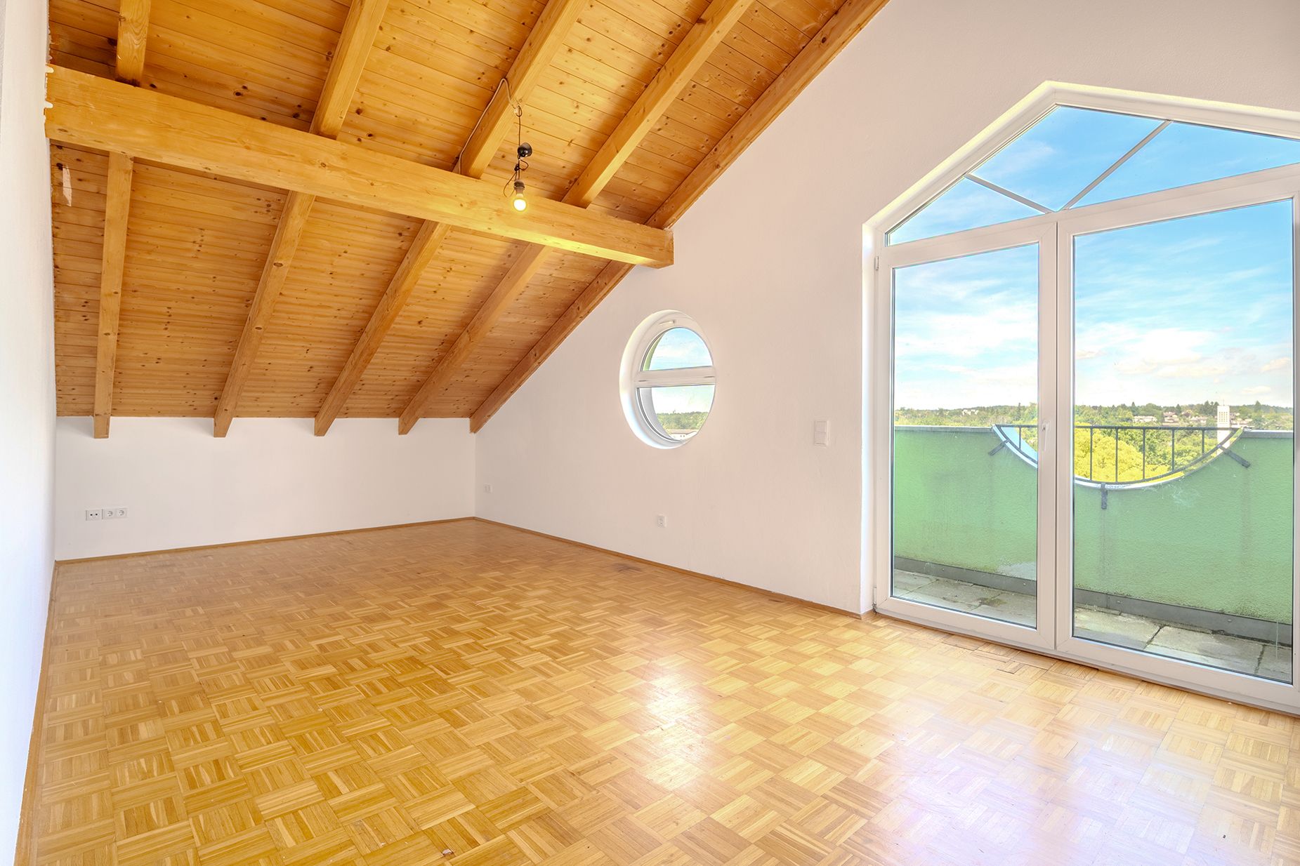 Helles Zimmer mit Holzdecke, rundem Fenster und Glastüren zu einem Balkon.