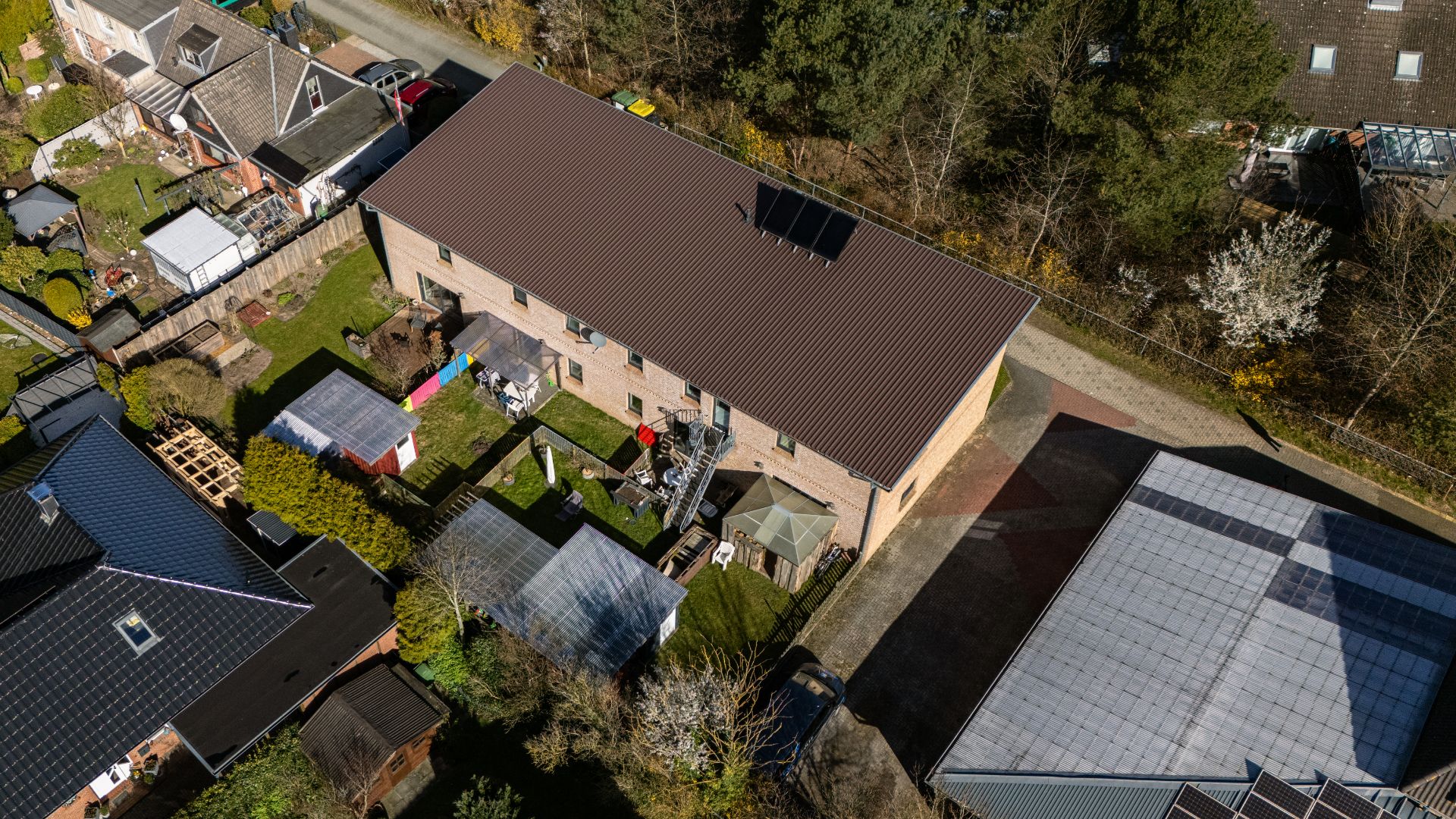 Luftaufnahme eines Wohnhauses mit Garten, Nebengebäuden und angrenzender Straße.