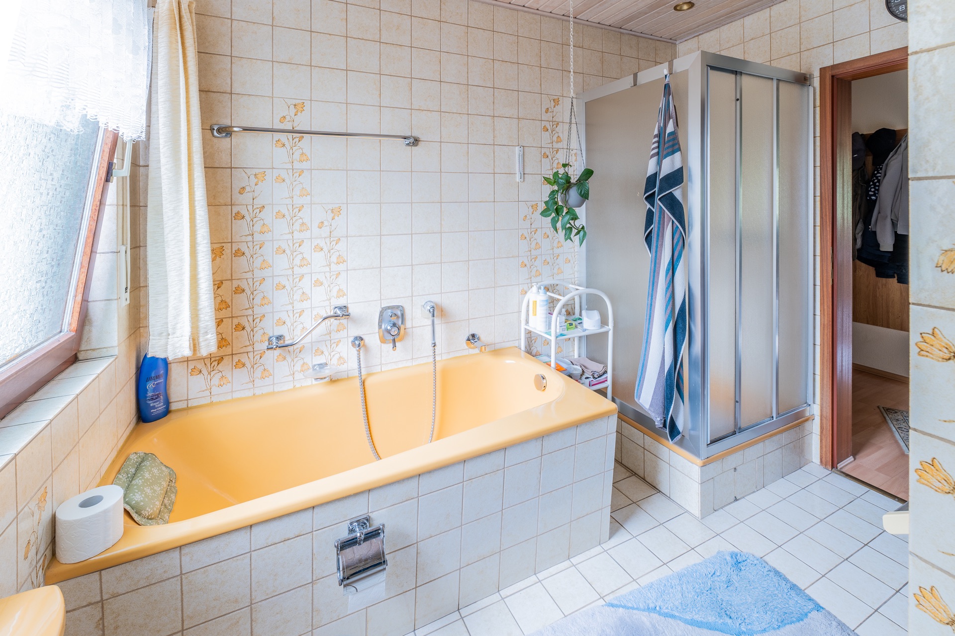 Badezimmer mit gelber Badewanne, Duschkabine, Fenster und Regal mit Handtüchern.