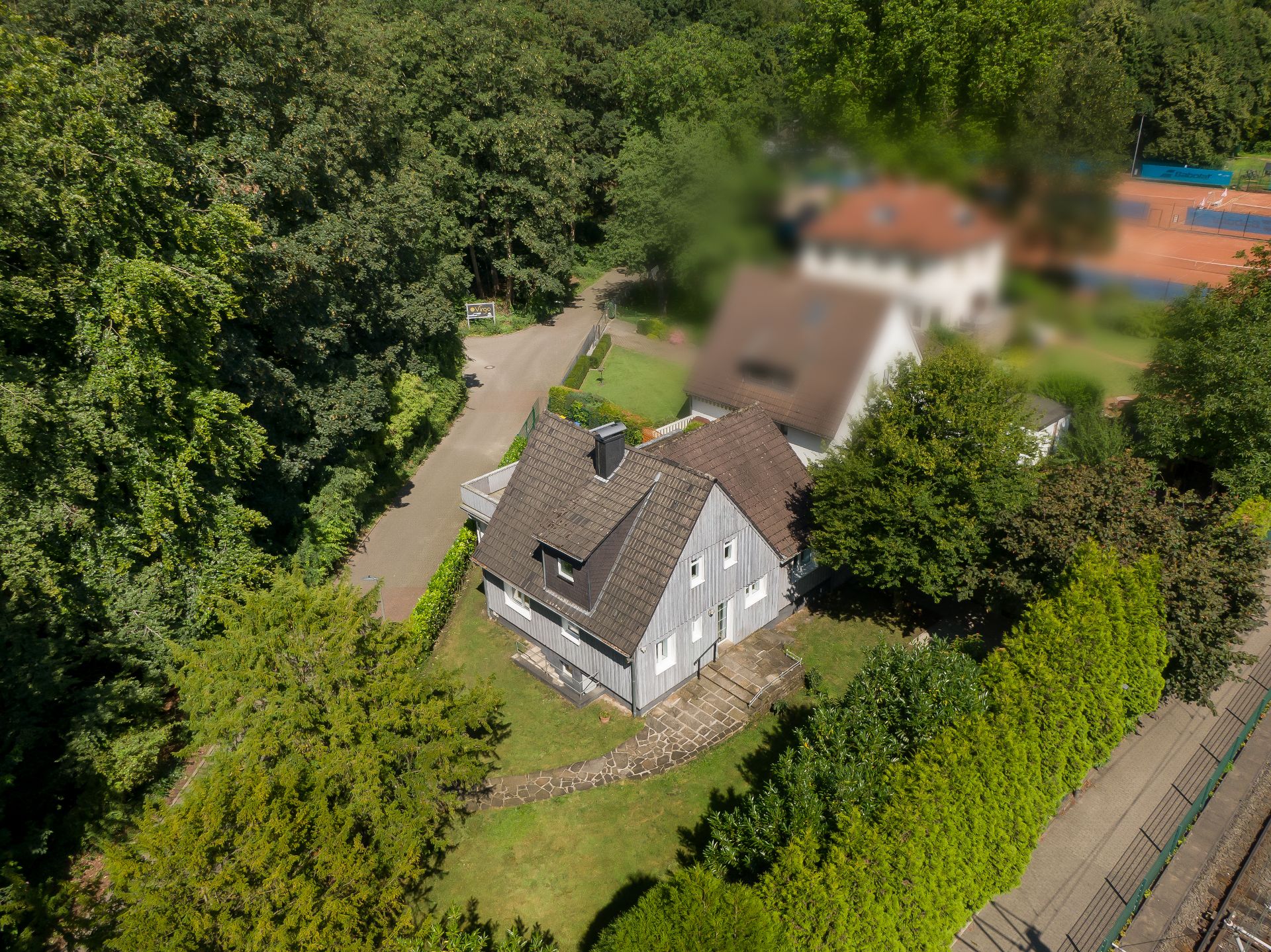 Luftaufnahme eines grauen Einfamilienhauses mit Garten und umliegenden Bäumen.