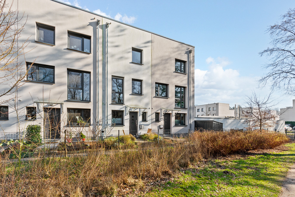 Moderne Reihenhäuser mit großen Fenstern und kleinen Vorgärten bei sonnigem Wetter.