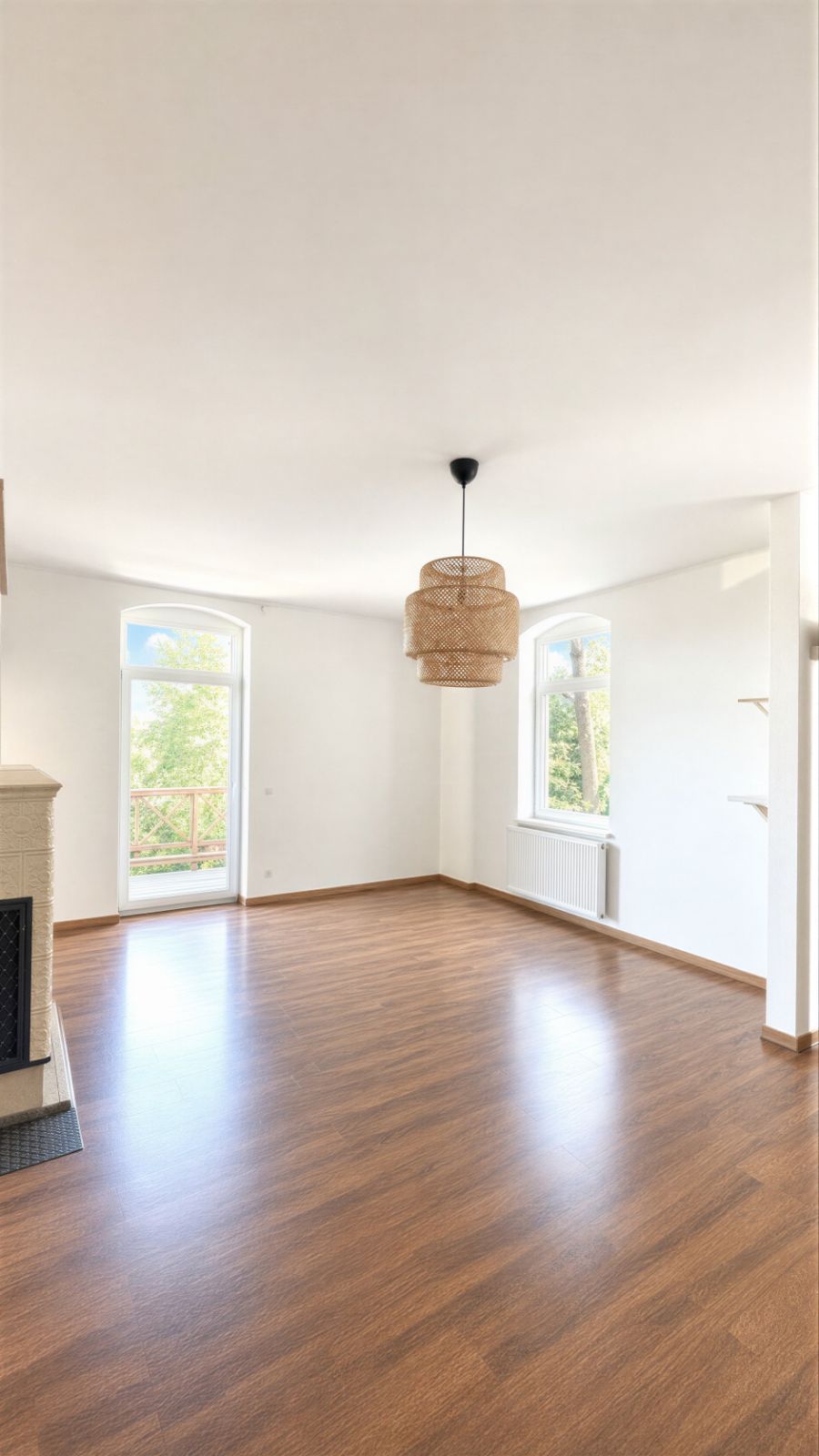 Helles Wohnzimmer mit Holzfußboden, großen Fenstern und einem Deckenlampenschirm.