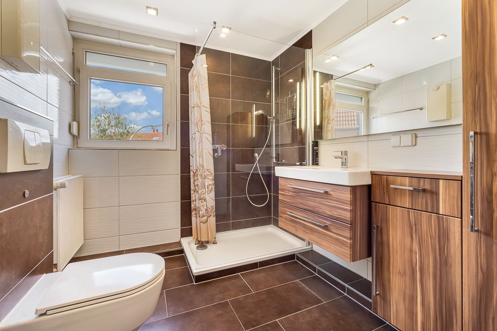 Modernes Badezimmer mit Dusche, Waschbecken, WC und Holzmöbeln, Fenster mit Blick nach draußen.
