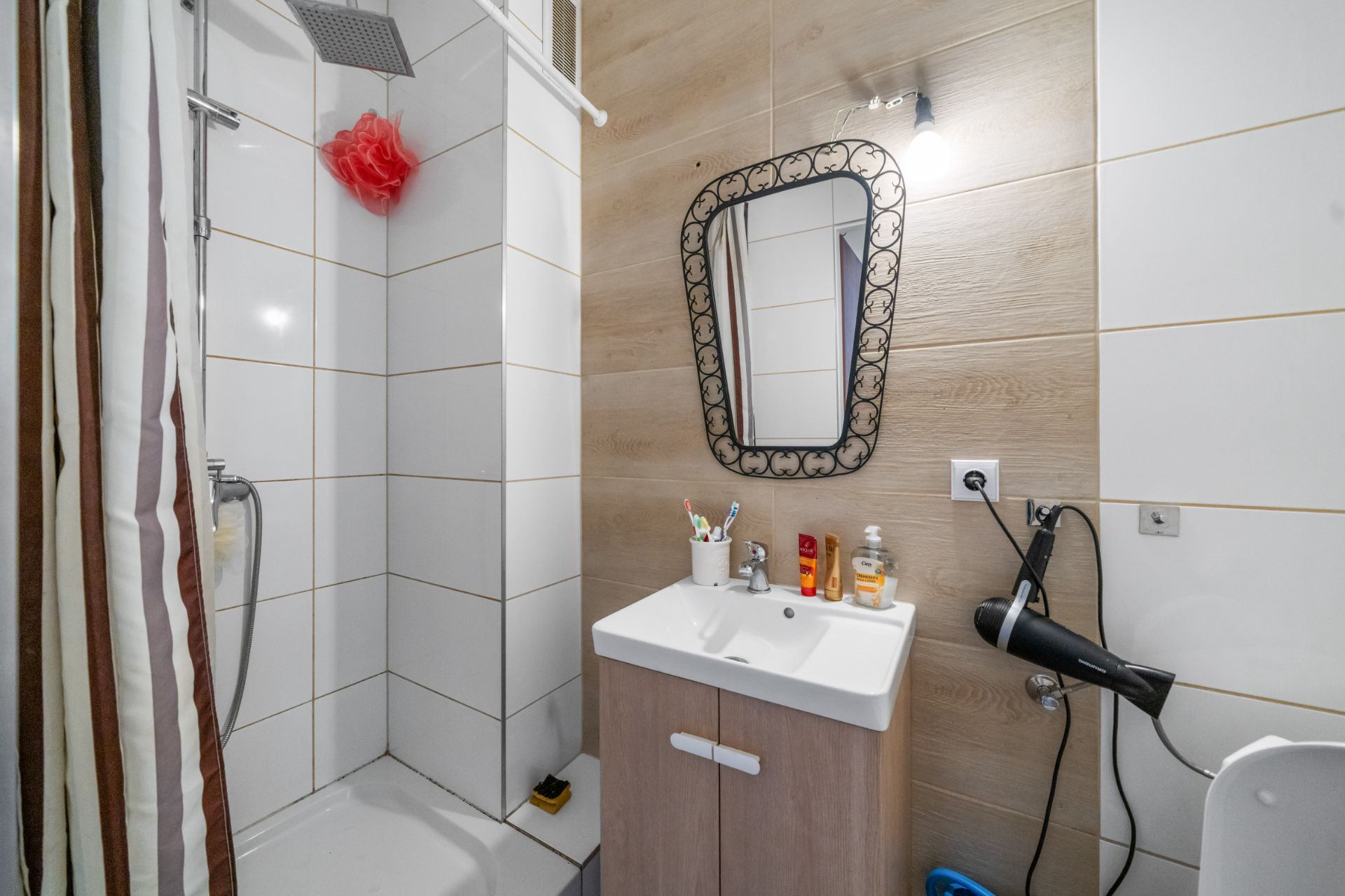 Modernes Bad mit Dusche, Waschbecken, Spiegel und an der Wand befestigtem Fön.