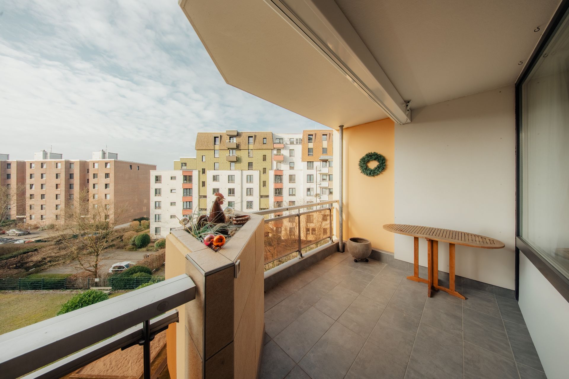 Balkon mit Tisch, Blumentopf und Blick auf Wohngebäude im Hintergrund.